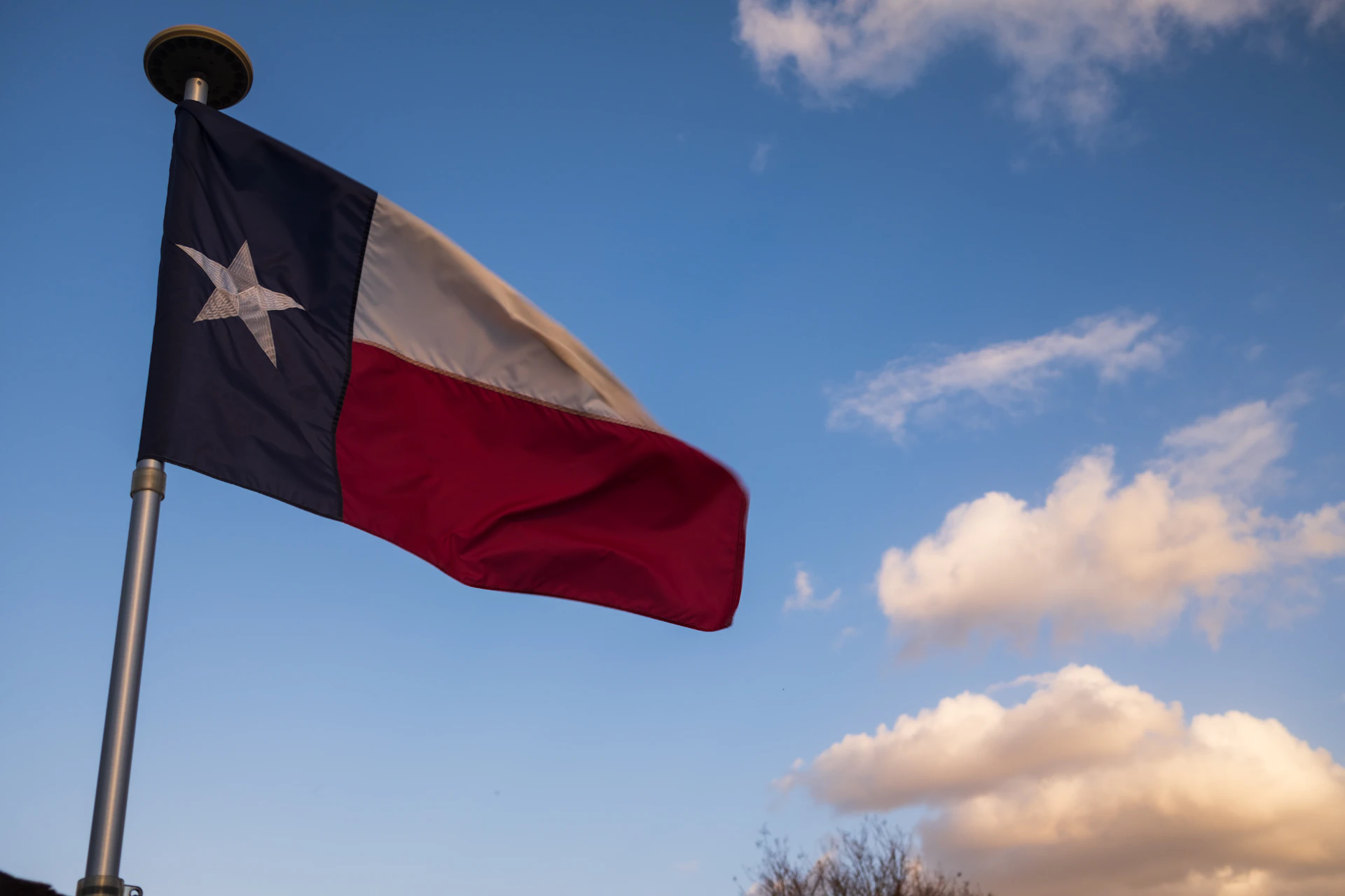 The texas flag waves against a blue sky.
