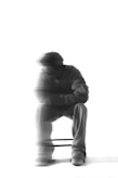 A man sits, blurred, in black and white.