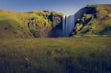A majestic waterfall cascades down a green hill.