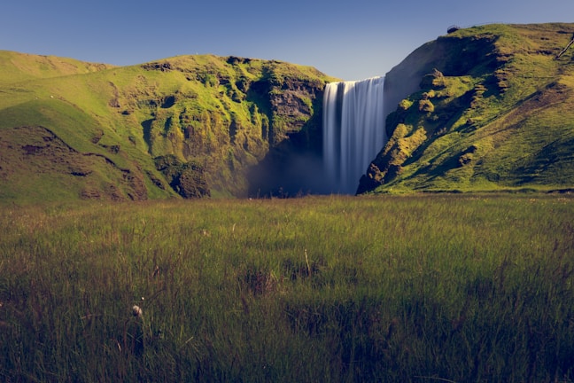 A majestic waterfall cascades down a green hill.