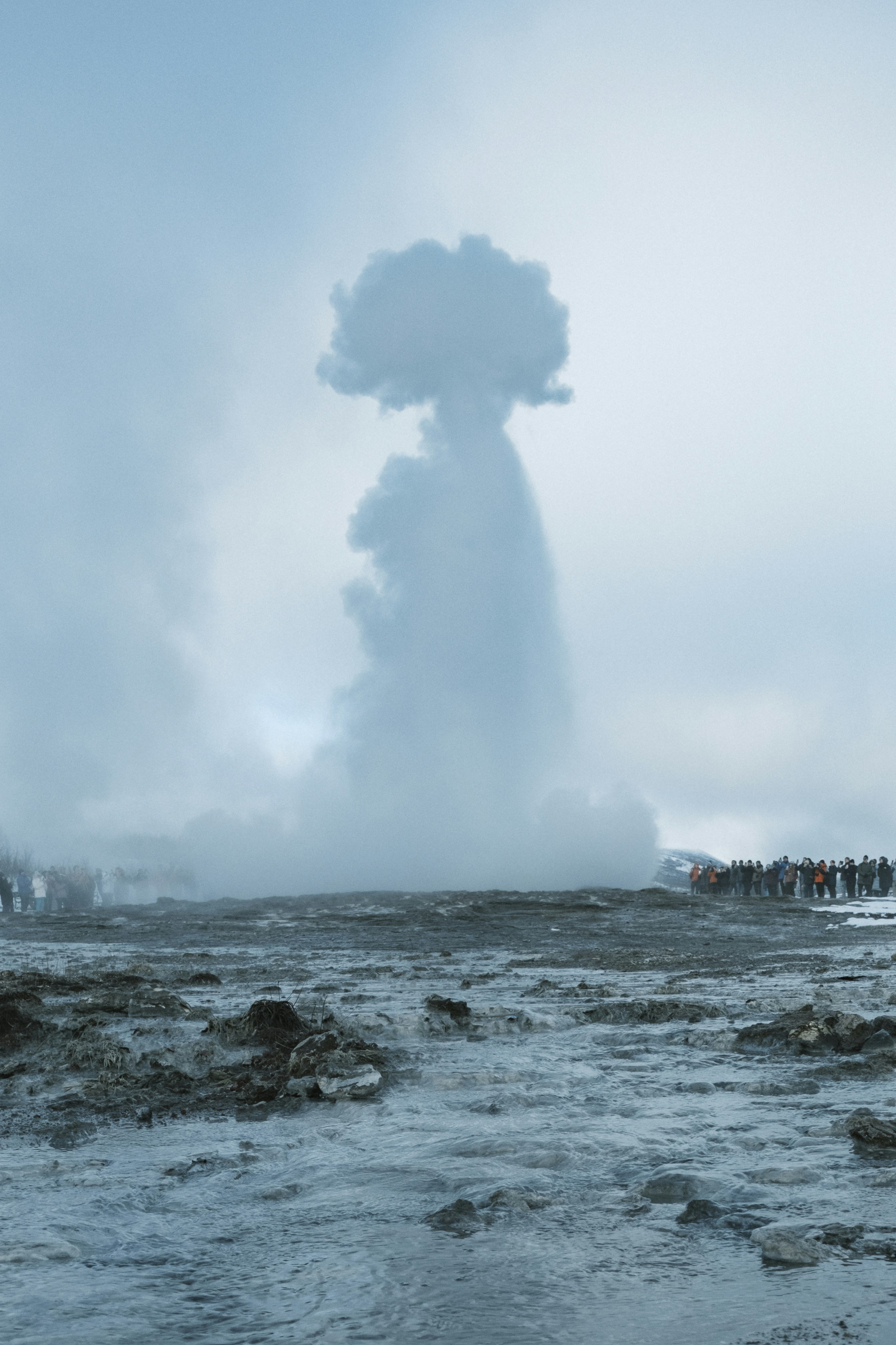 A geyser erupts, impressing many onlookers.