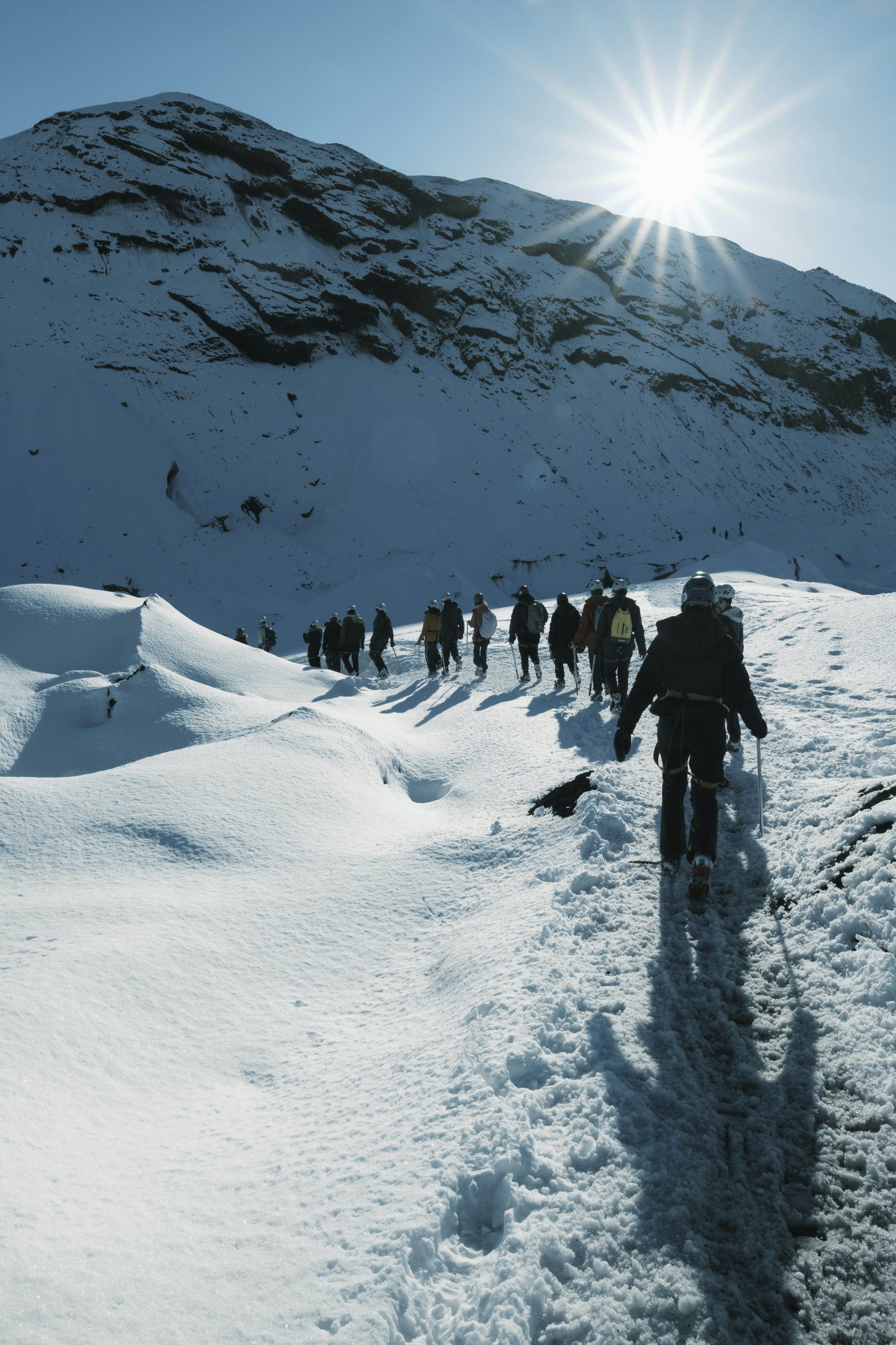 Hikers walk in snow, toward the bright sun.