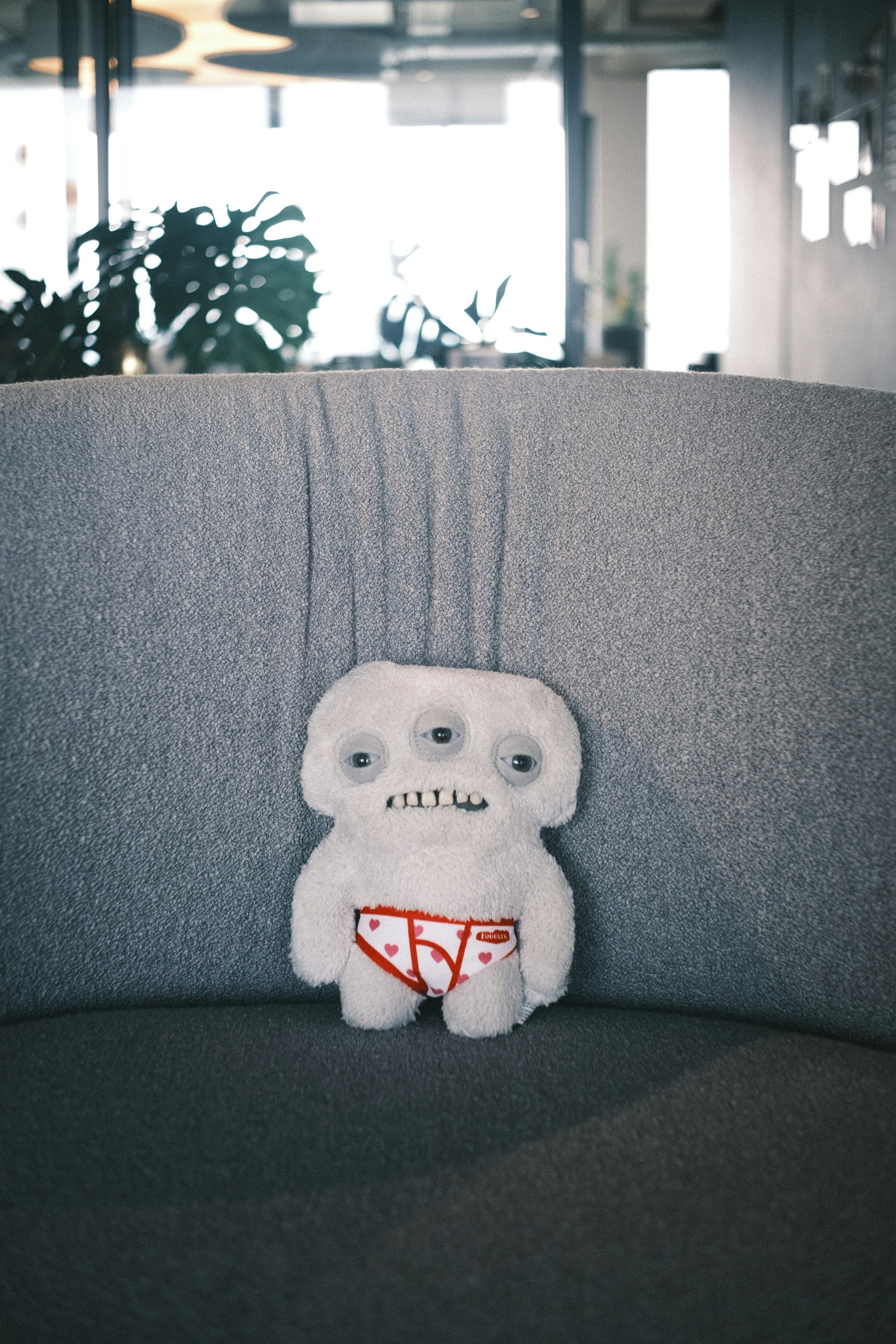 A three-eyed monster plush doll sits on a couch.
