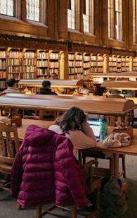 Students study in a library with bookshelves.