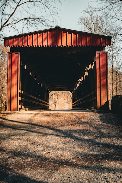 A red covered bridge stands in a sunlit forest.