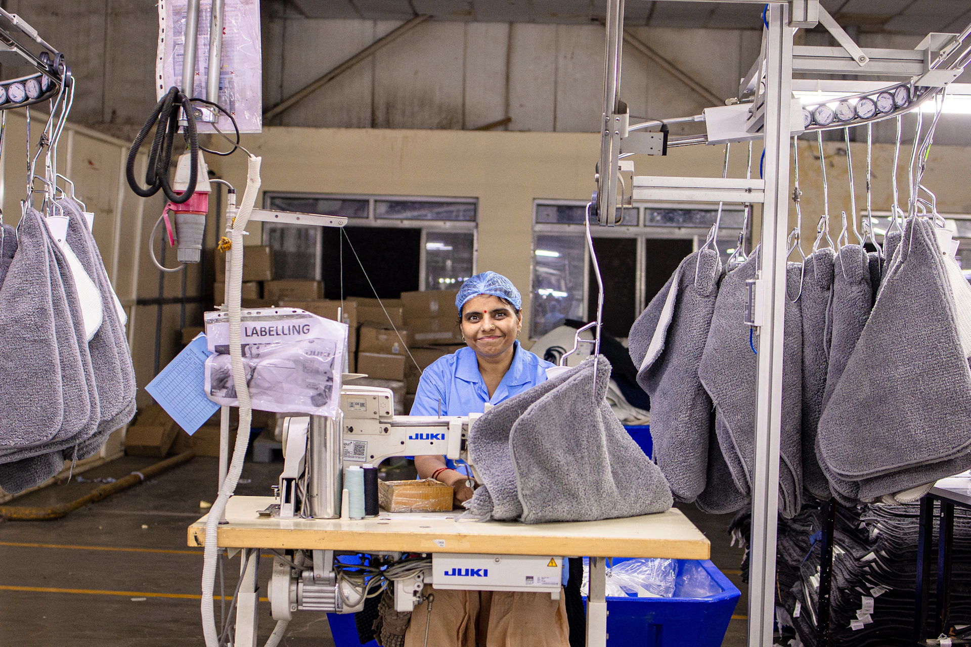 A seamstress smiles while sewing in a factory.
