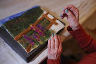 Person is making felt artwork of a landscape.