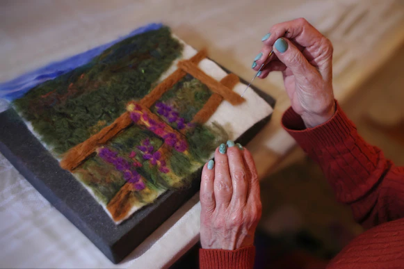 Person is making felt artwork of a landscape.