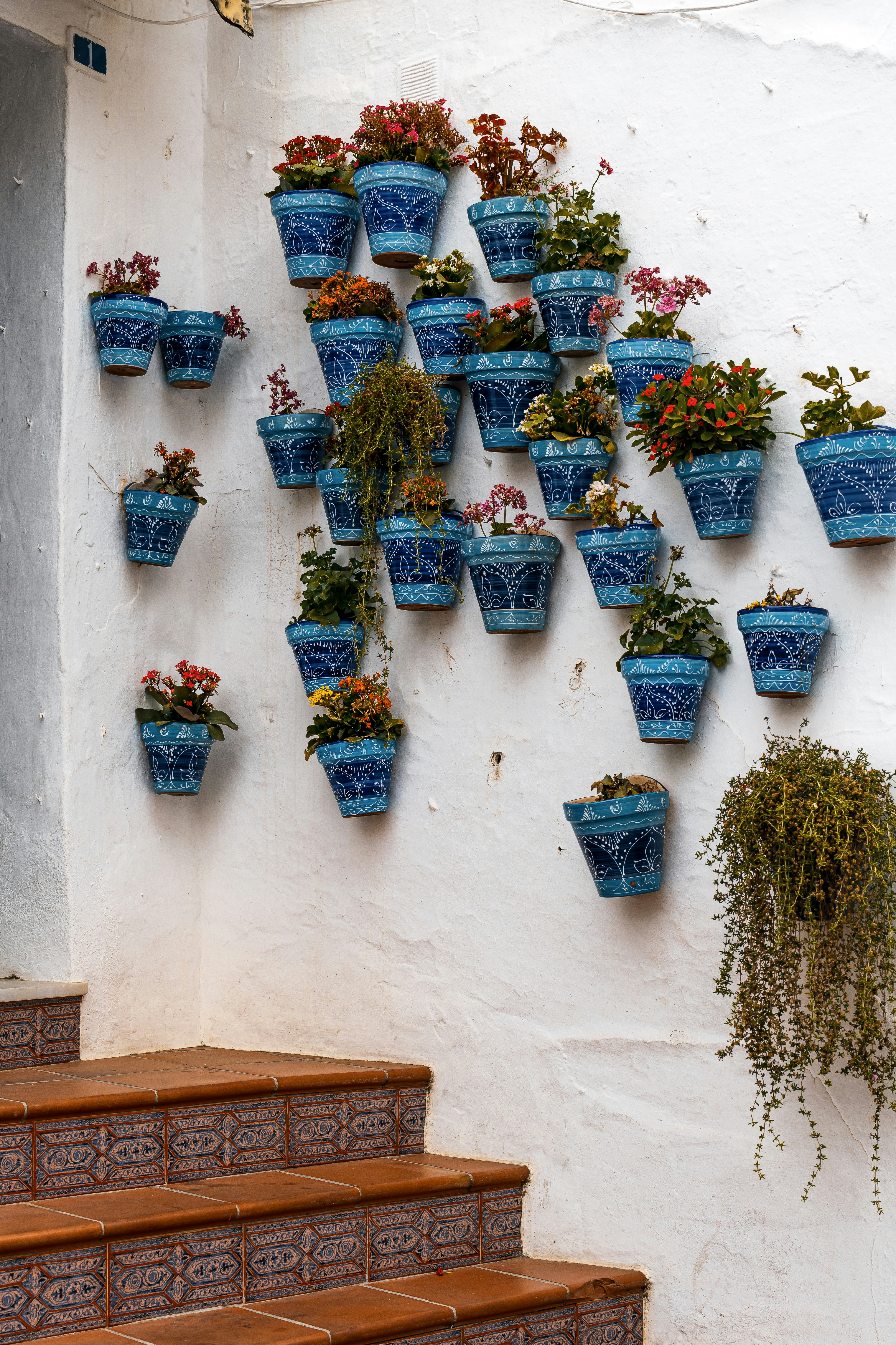 Macetas azules decoran una pared y escaleras blancas.