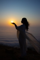 Woman holds the sun in her hand at sunrise.