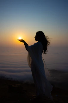 Woman holds the sun over a sea of clouds