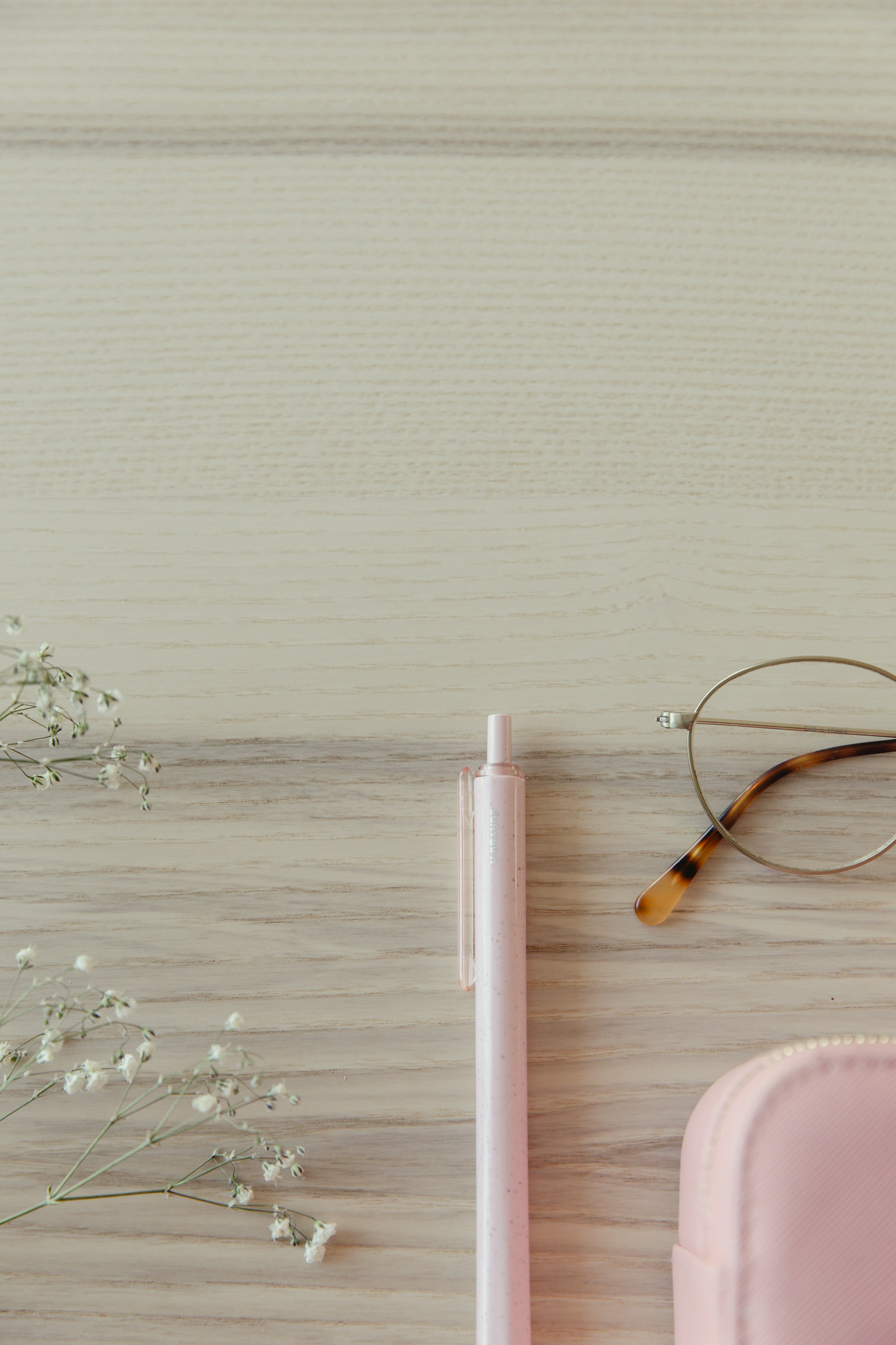 Pink stationary, glasses, and flowers on wood.