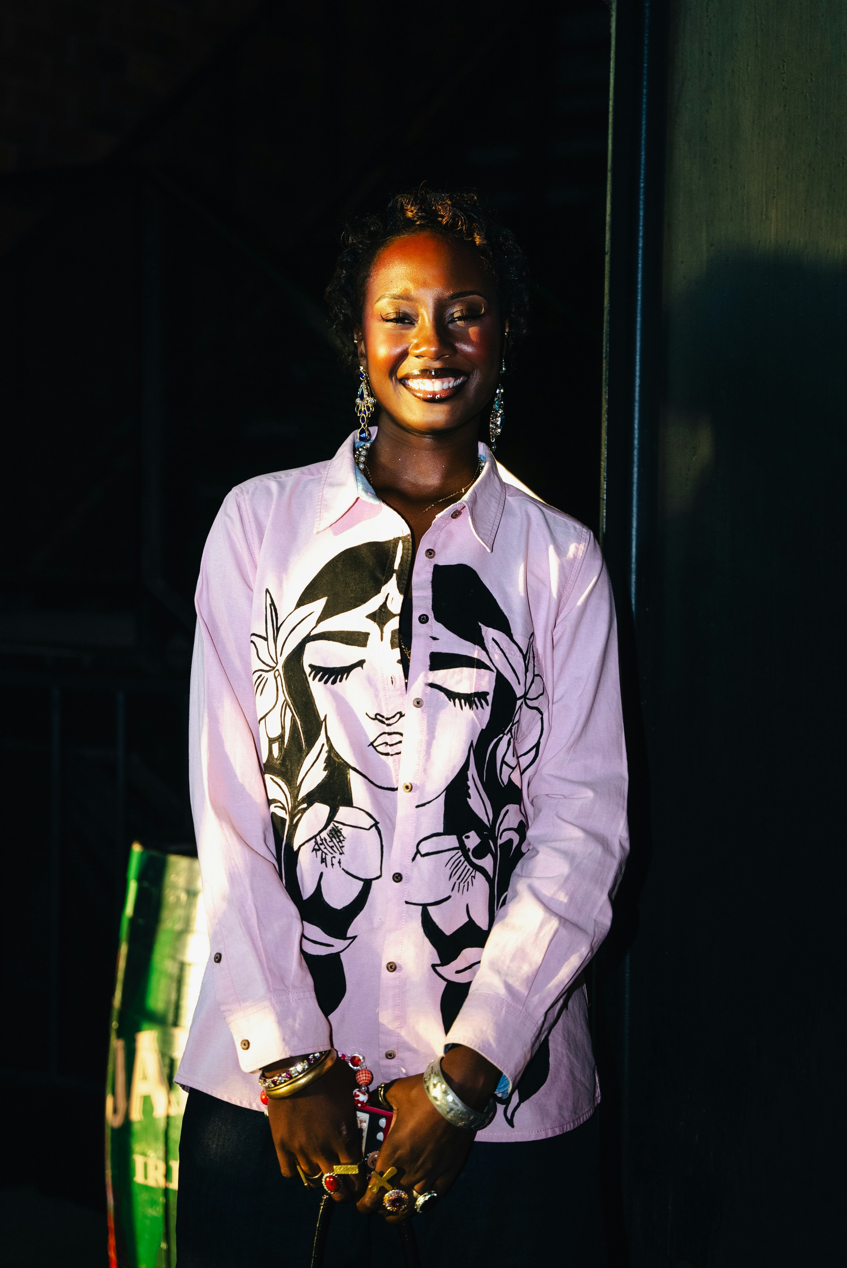 A smiling woman wears a stylish, pink shirt.