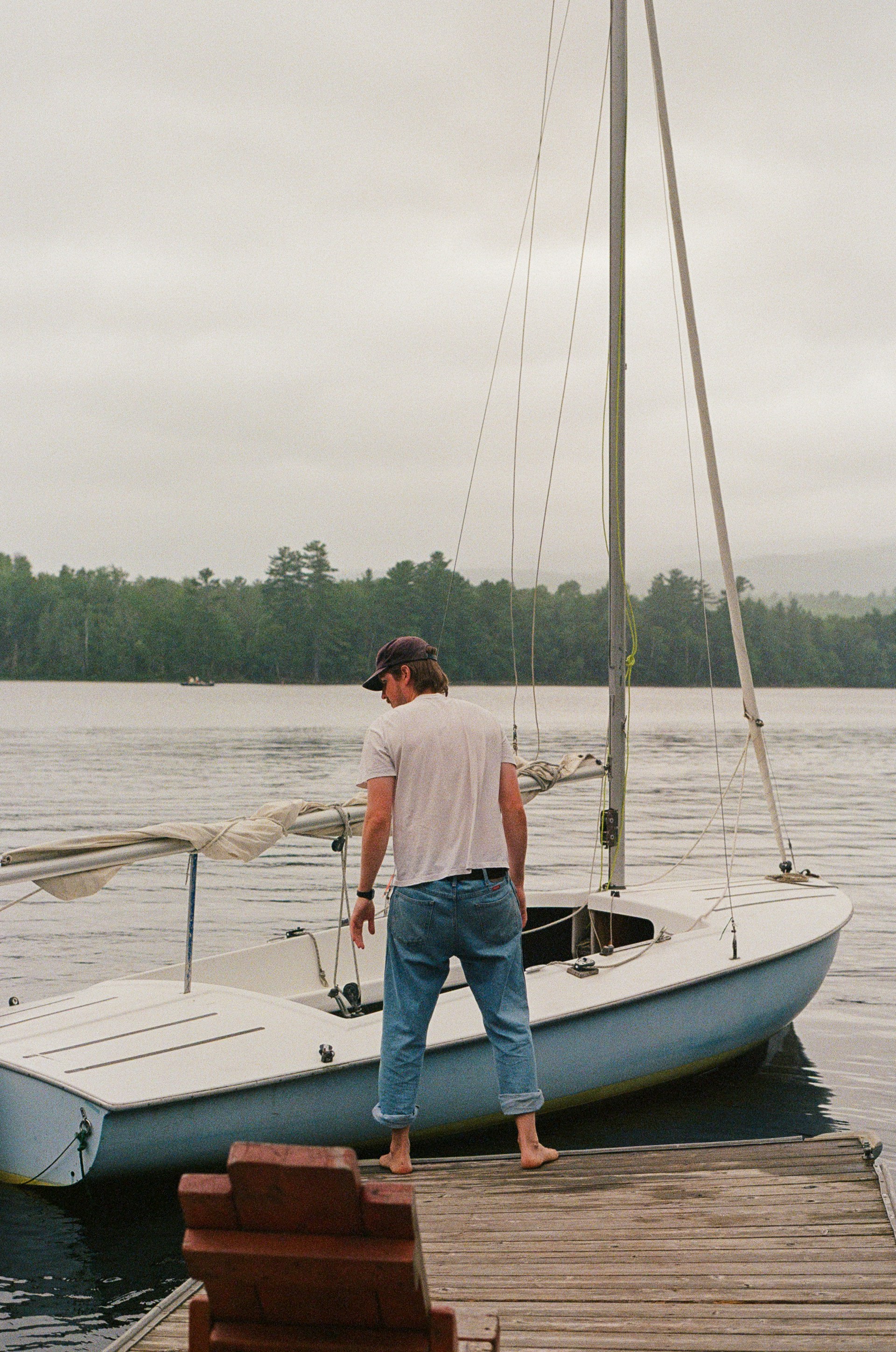 Man standing next to his sailboat at the dock.