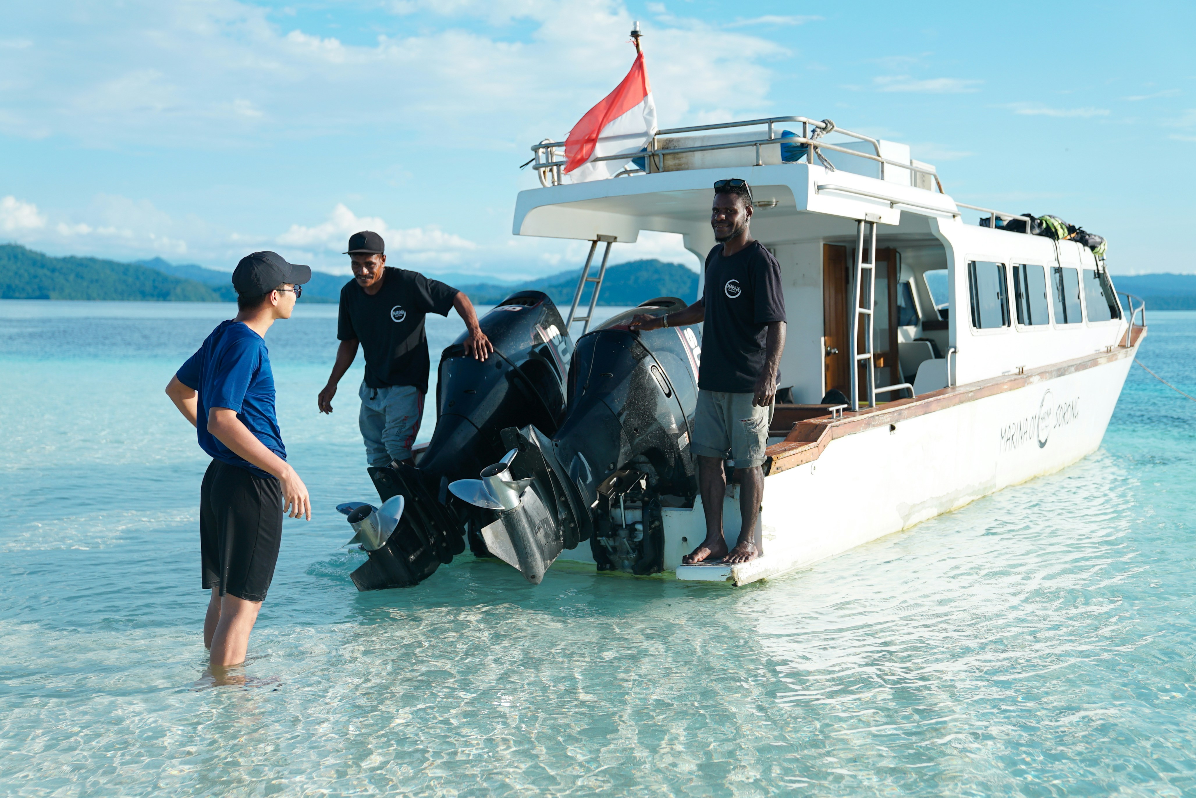 People stand near a boat in the ocean.