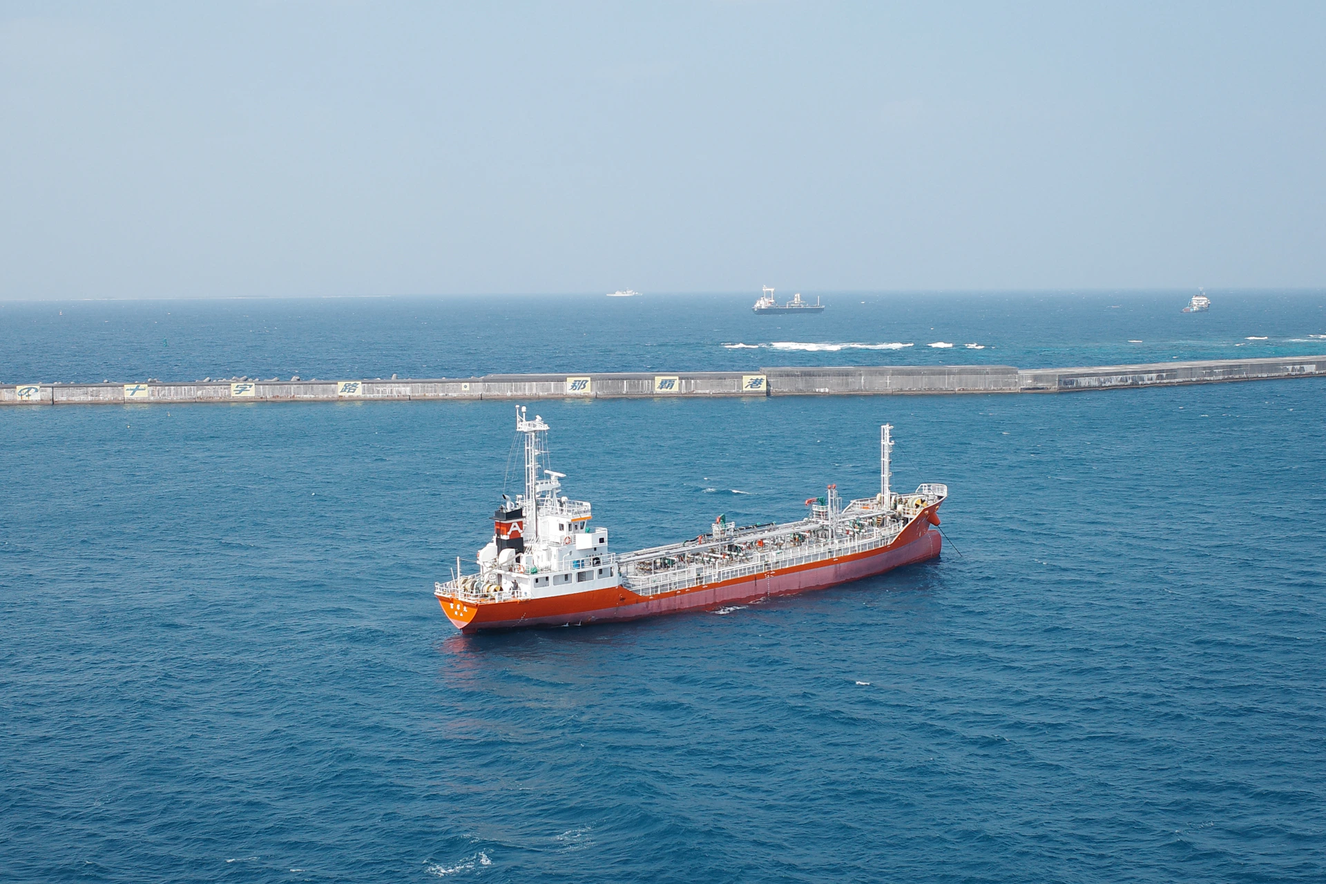 A red ship sails on the calm, blue ocean