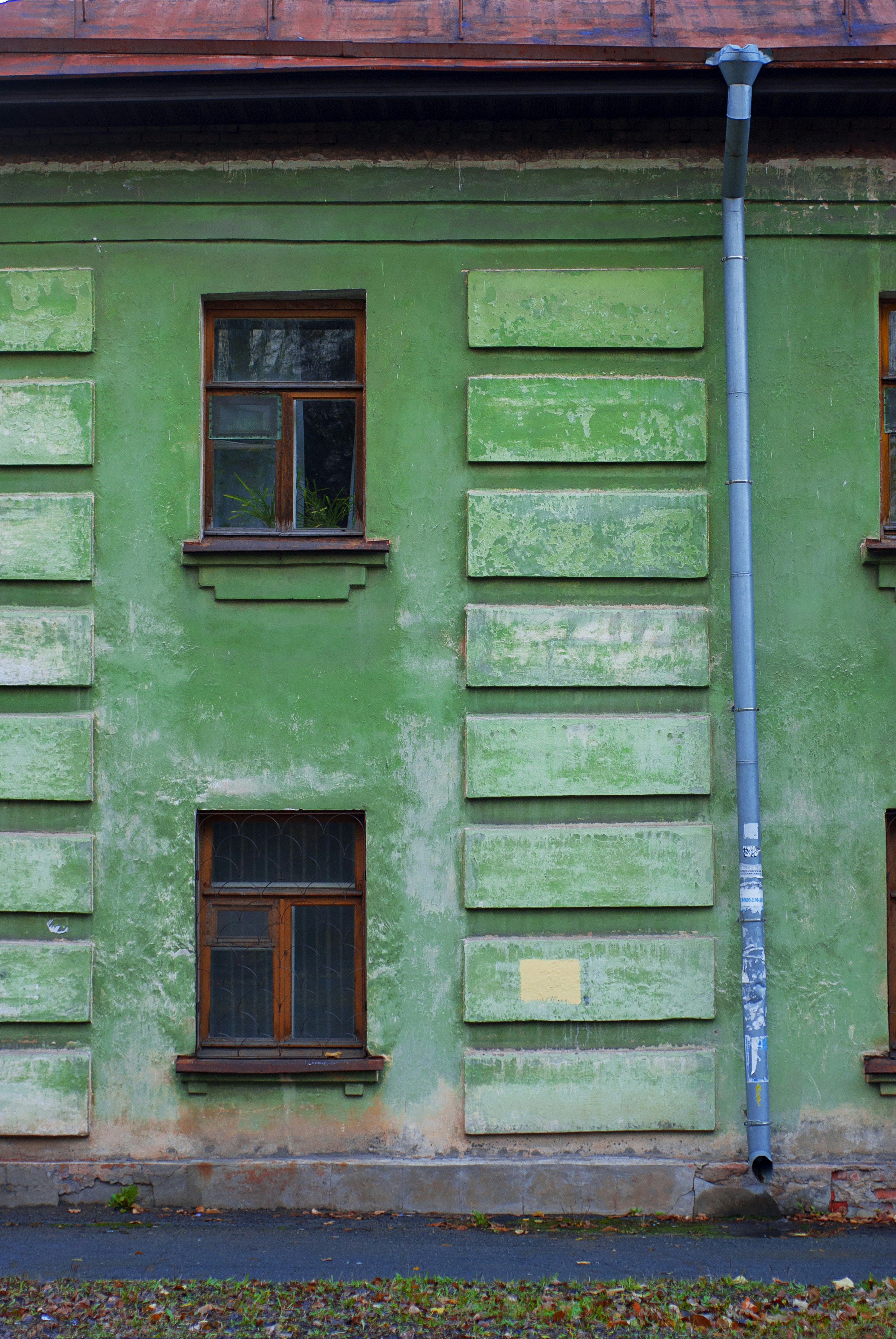A weathered green building with windows and a pipe.