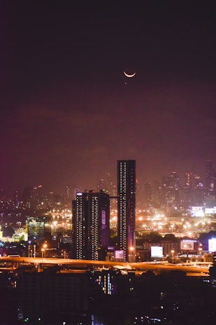 City skyline illuminated at night with a crescent moon.