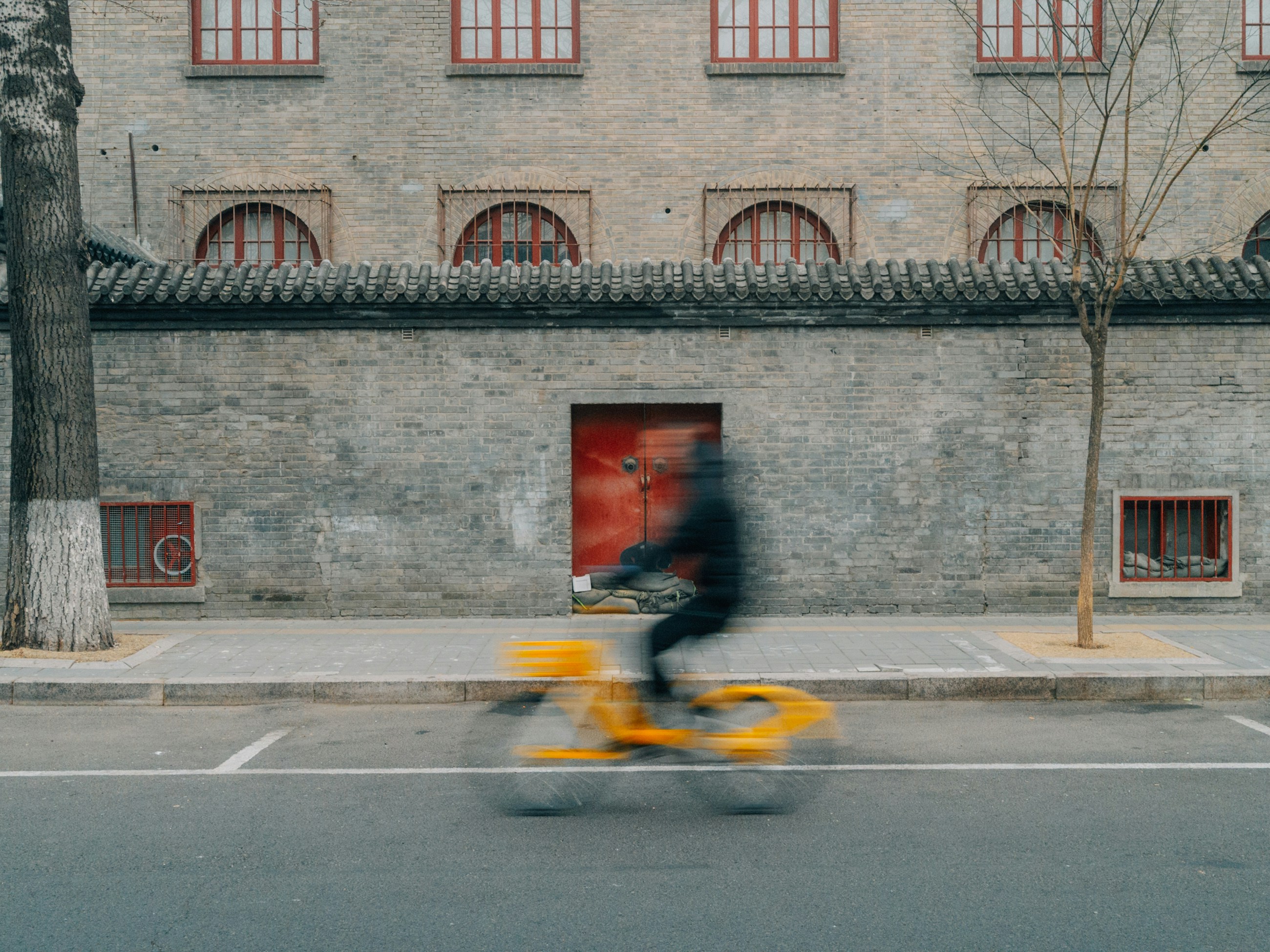 Blurred cyclist rides past an old brick building.