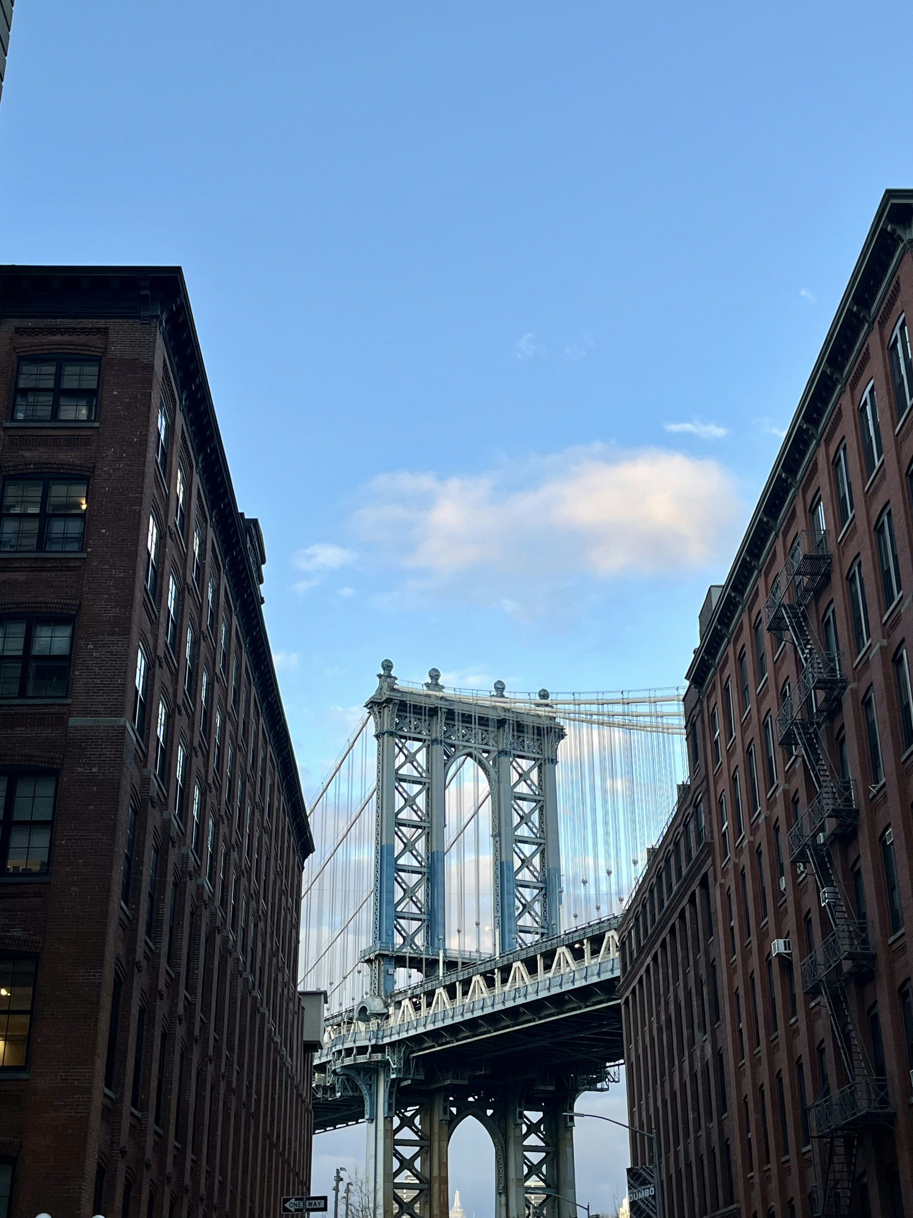 The manhattan bridge is framed between buildings.