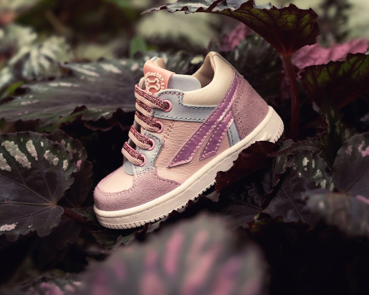 Pink toddler sneaker styled among dark leafy plants