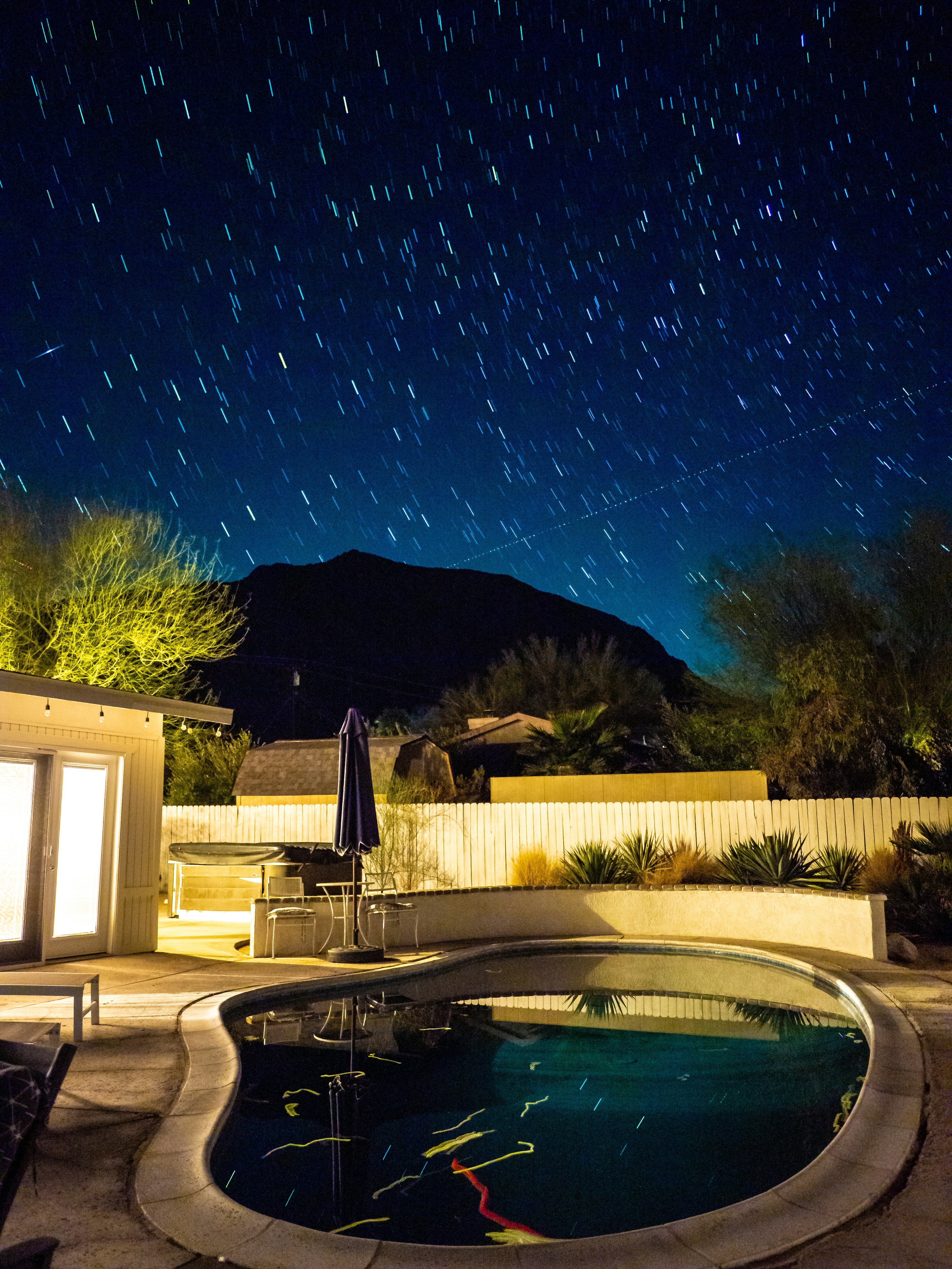 Star trails over a pool with mountains at night