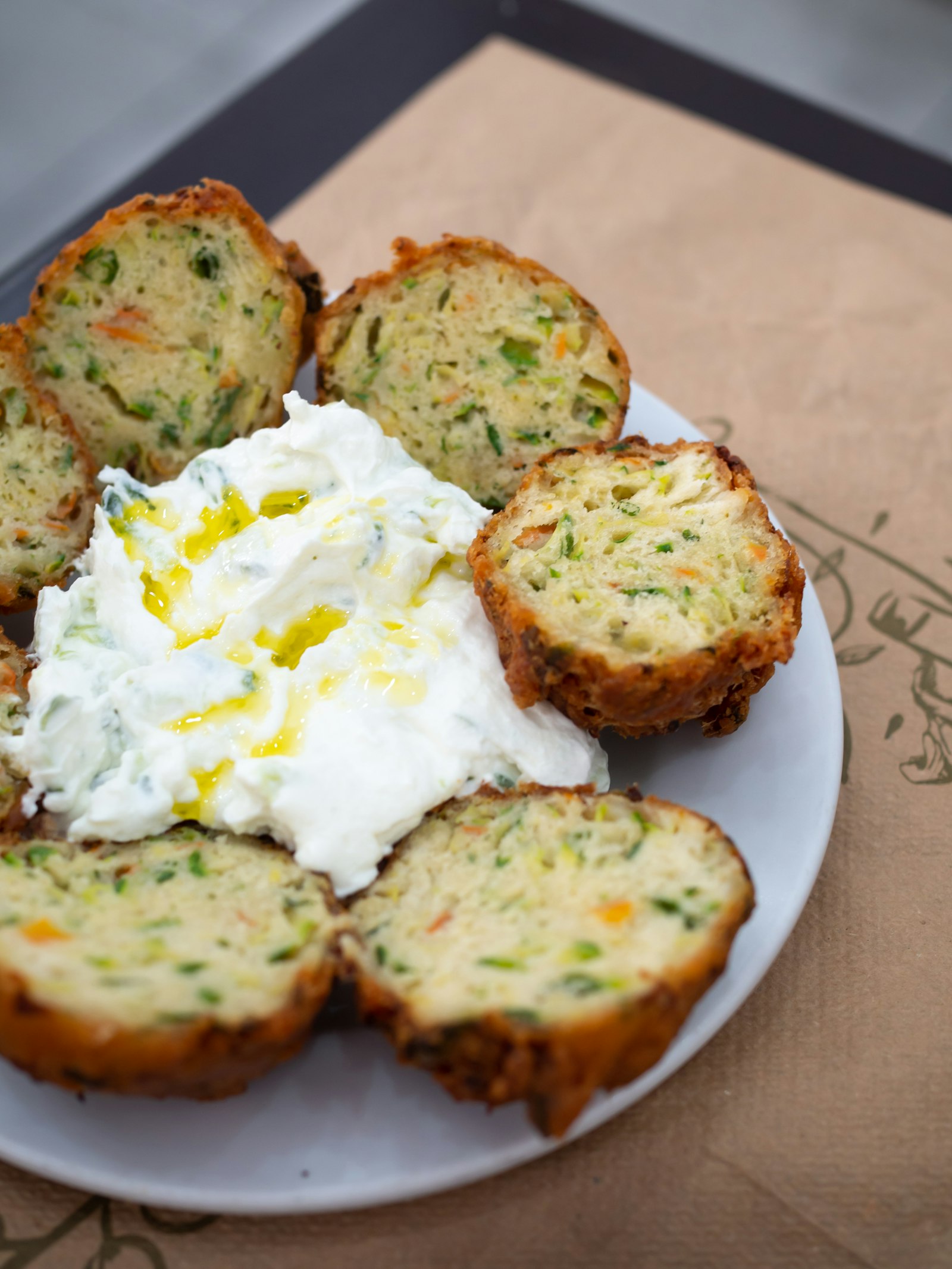 Golden zucchini and herb fritters on a white plate with a creamy yogurt dip and olive oil