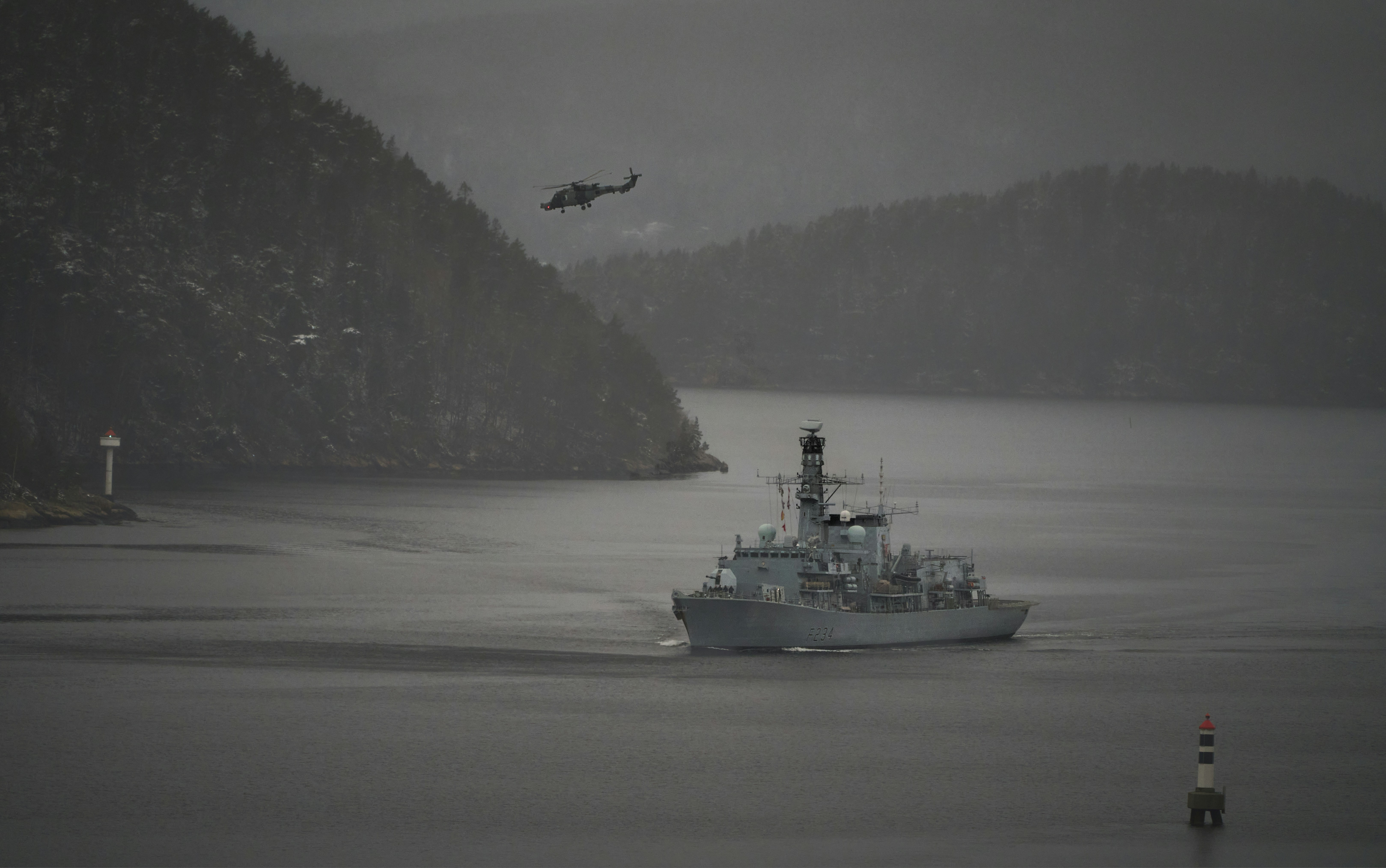 A naval ship sailing with helicopter overhead.