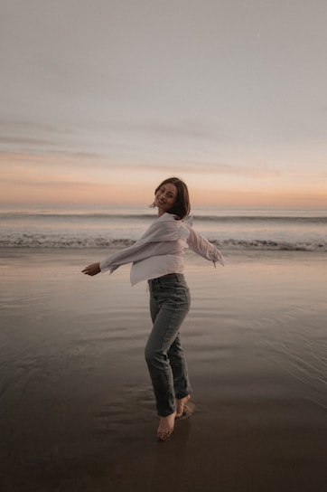 Woman happily spins on a beach at sunset.
