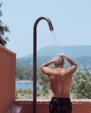 Man enjoys an outdoor shower with scenic views.