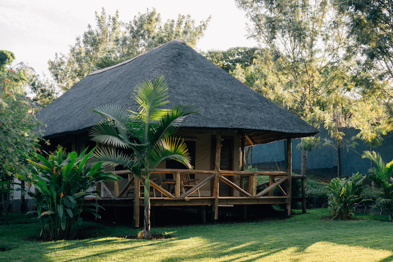 A thatched-roof banda lodge bungalow on a green lawn in East Africa