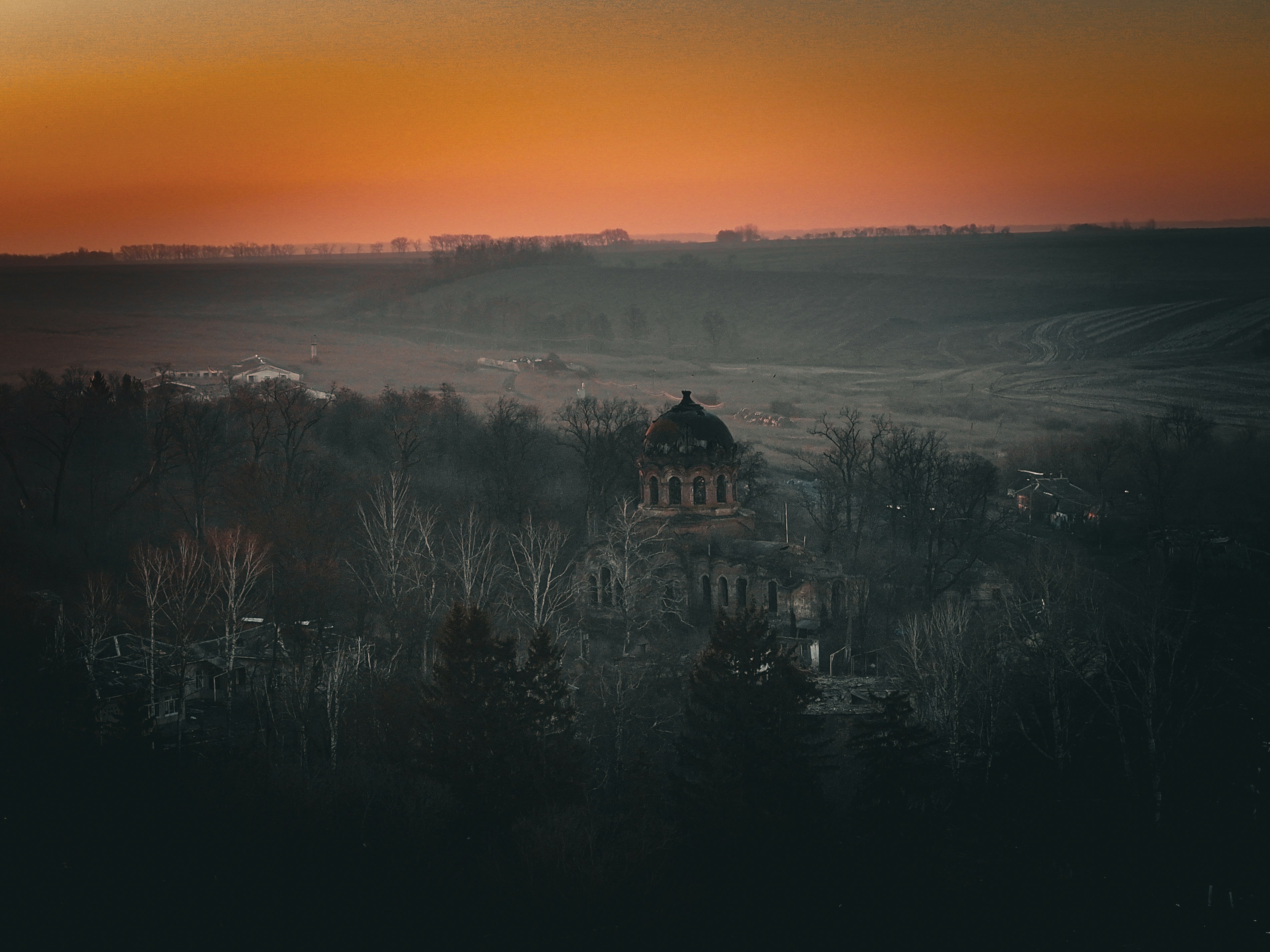Orange sky above a dark landscape with a building.