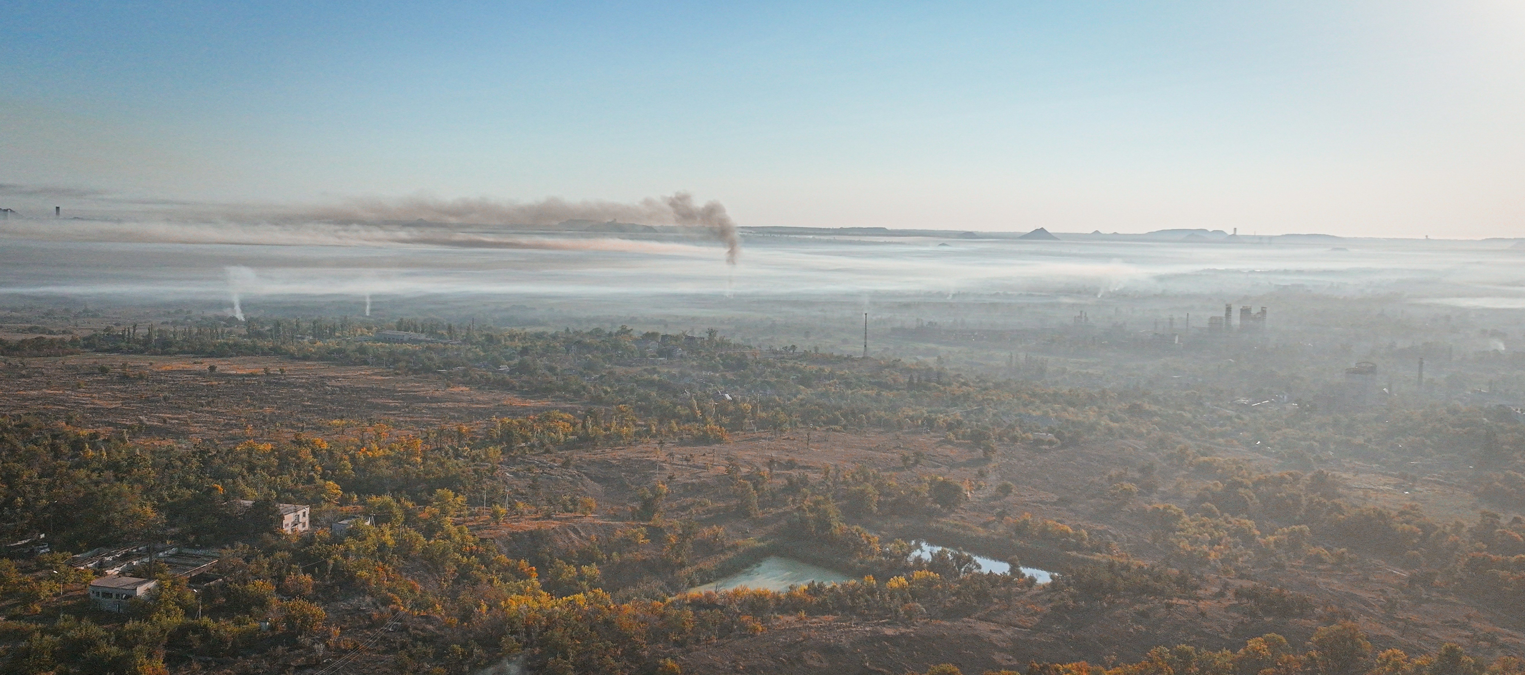 Vast landscape with fog, forest, and smoke in the sky.