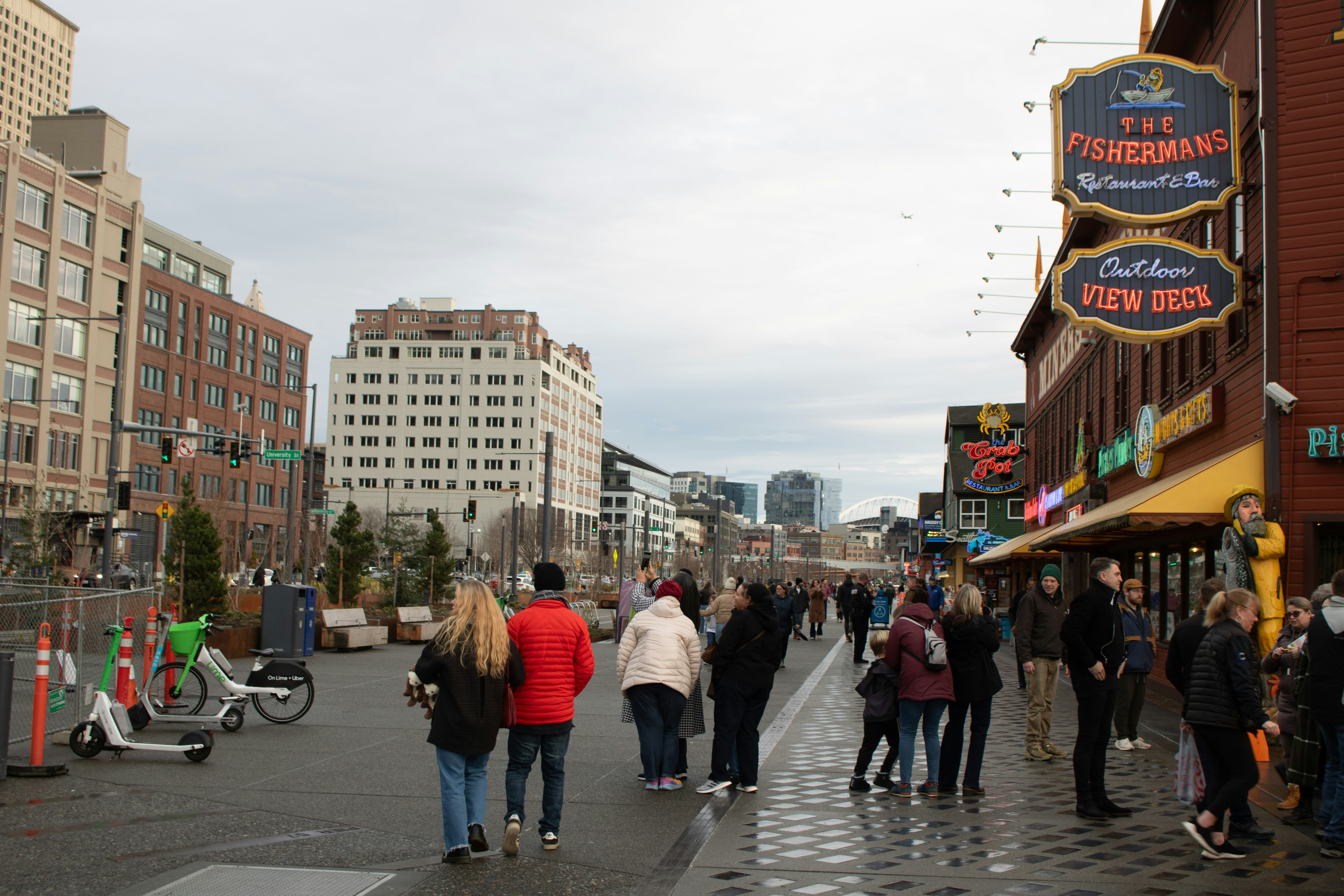 People walk along a city boardwalk with buildings.