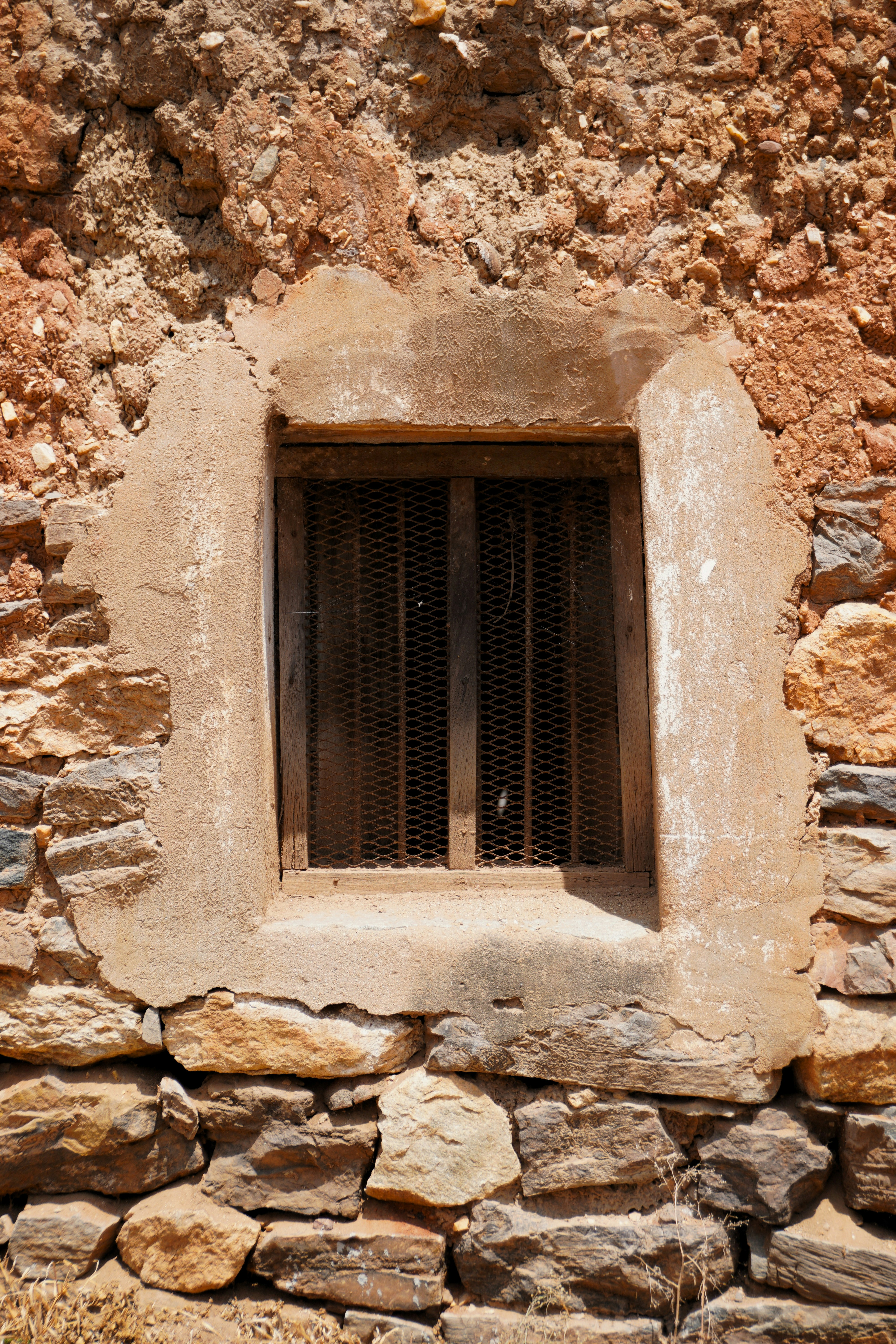 A window with a grille is built into a stone wall.