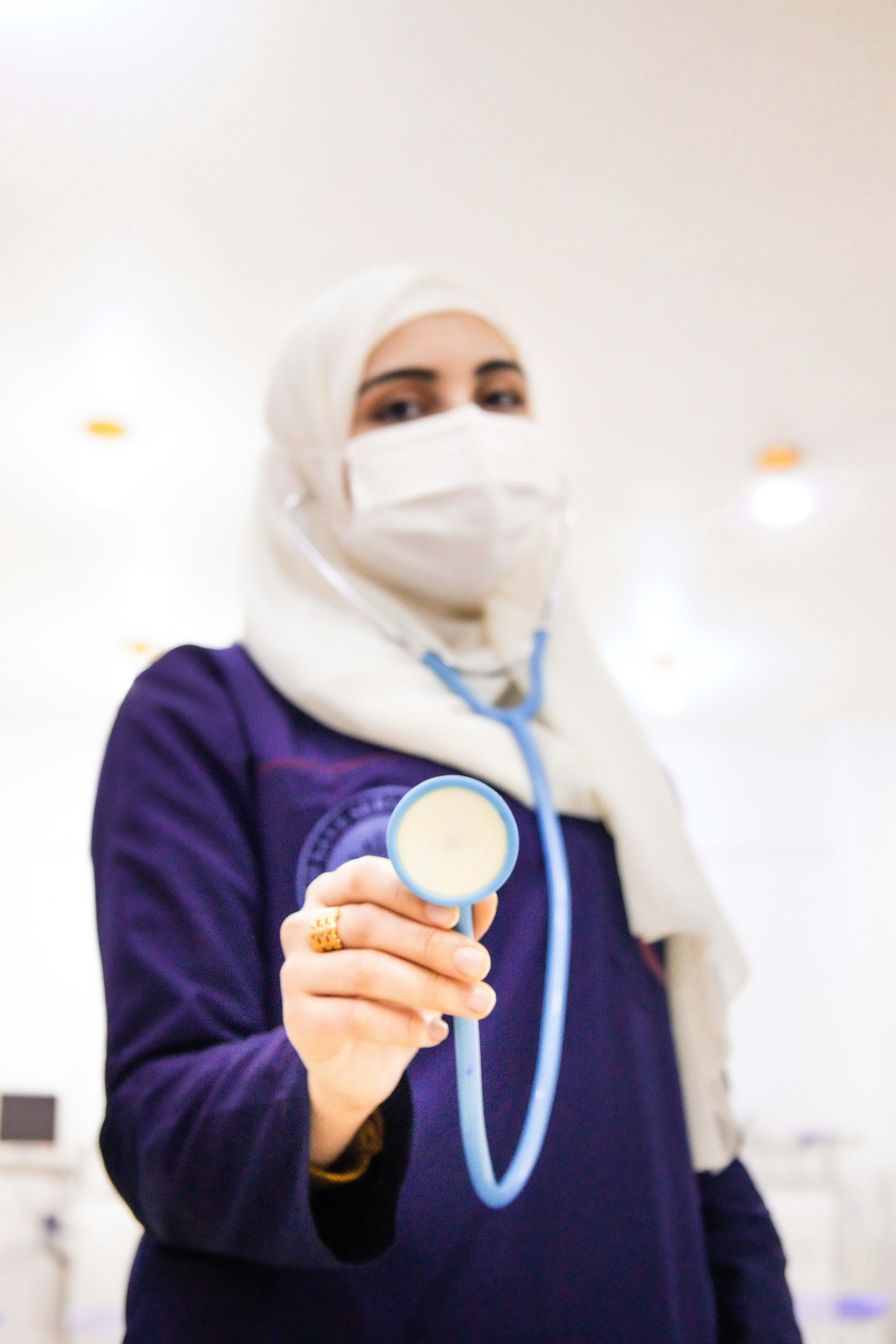 A Syrian doctor stands in the middle of the picture, holding a stethoscope to check the patient's pulse and placing it on the camera. طبيبة سورية تقف في منتصف الصورة وتمسك سماعة طبية لفحص نبض المريض وتضعها على الكاميرا