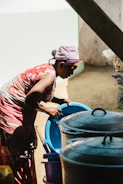 Woman washes dishes outdoors near cooking pots.