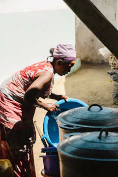 Woman washes dishes outdoors near cooking pots.
