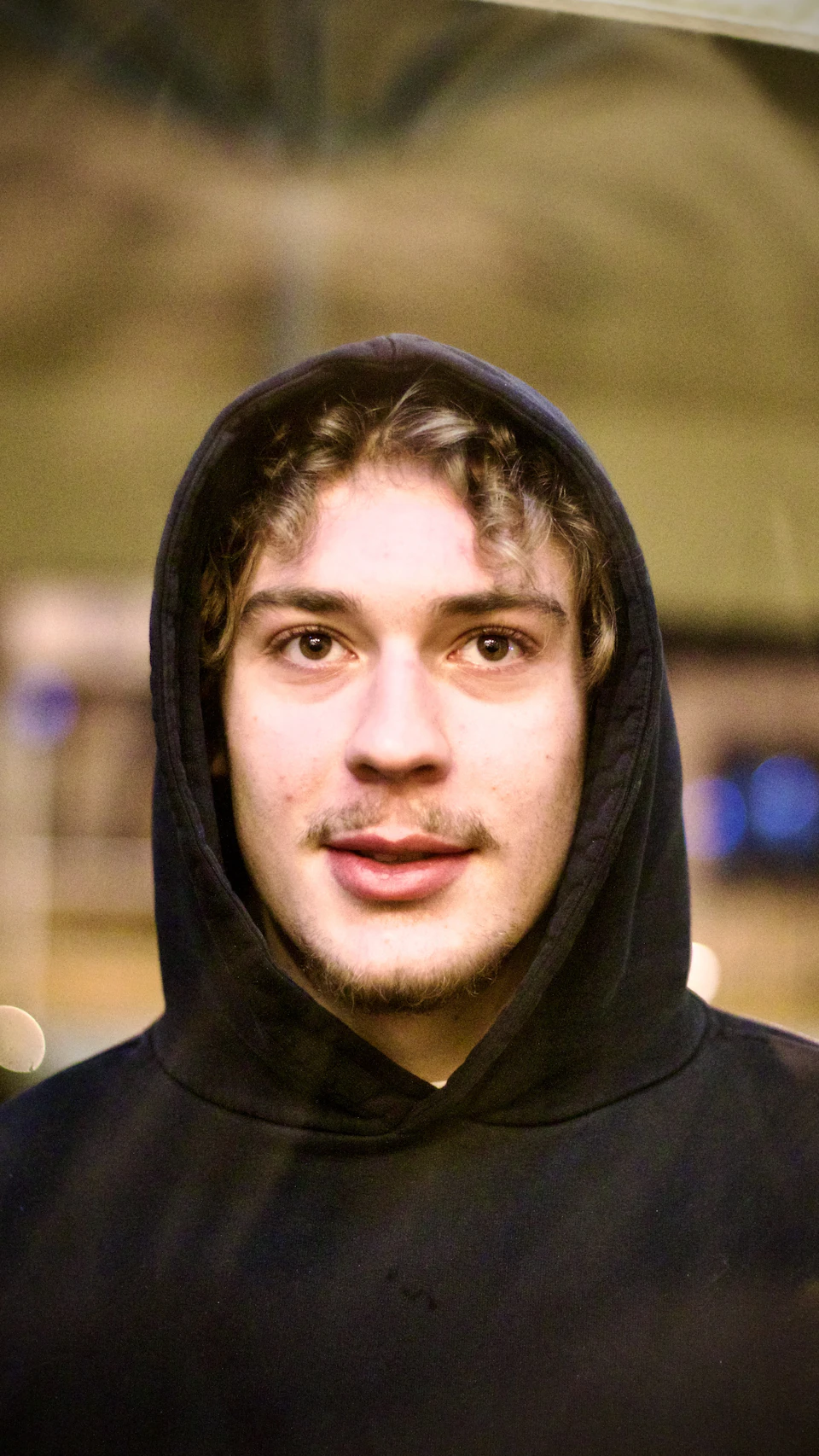 Young man wearing a black hoodie with partially obscured face in blurry background