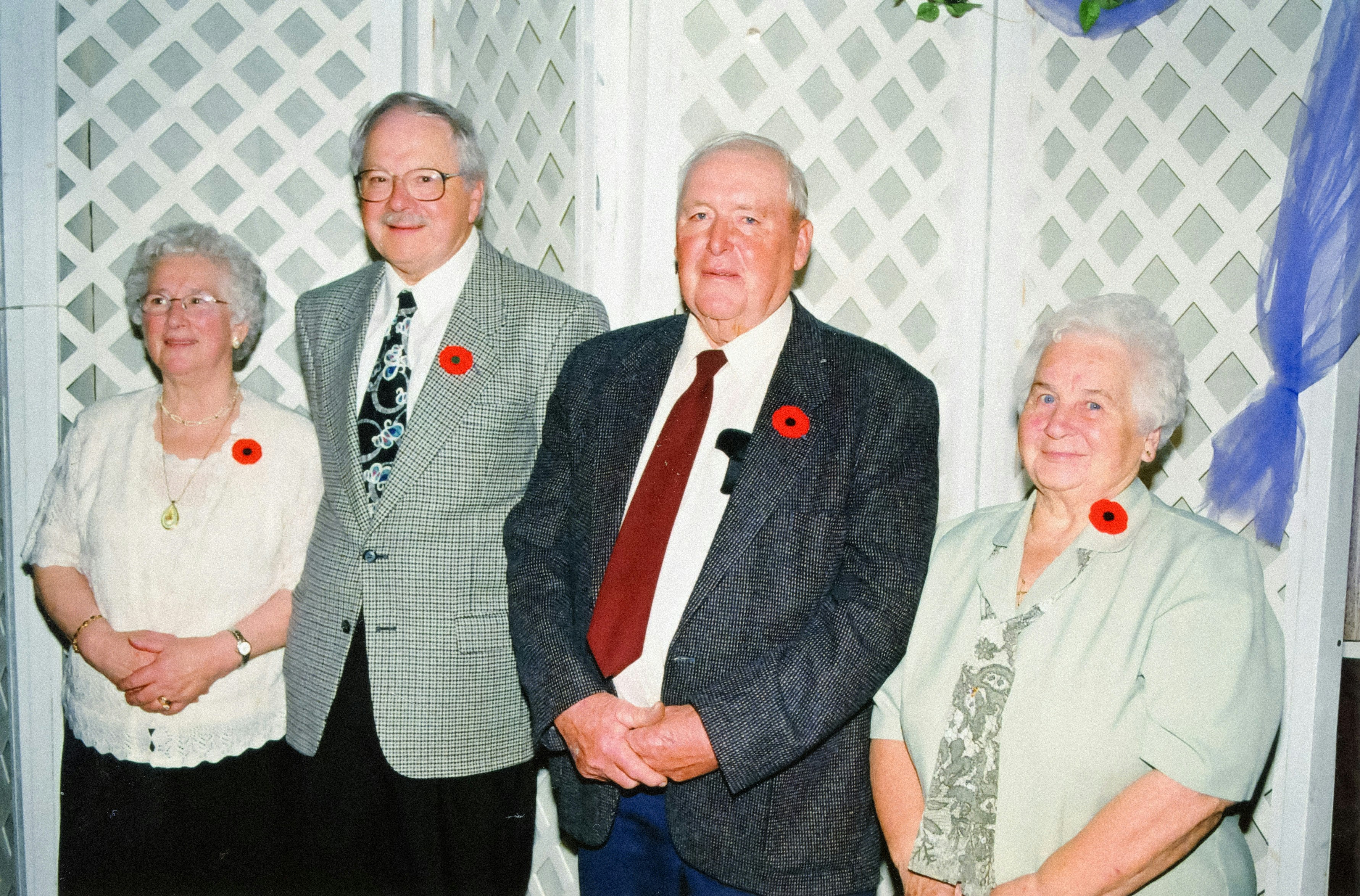 Four people wearing red poppies stand together.