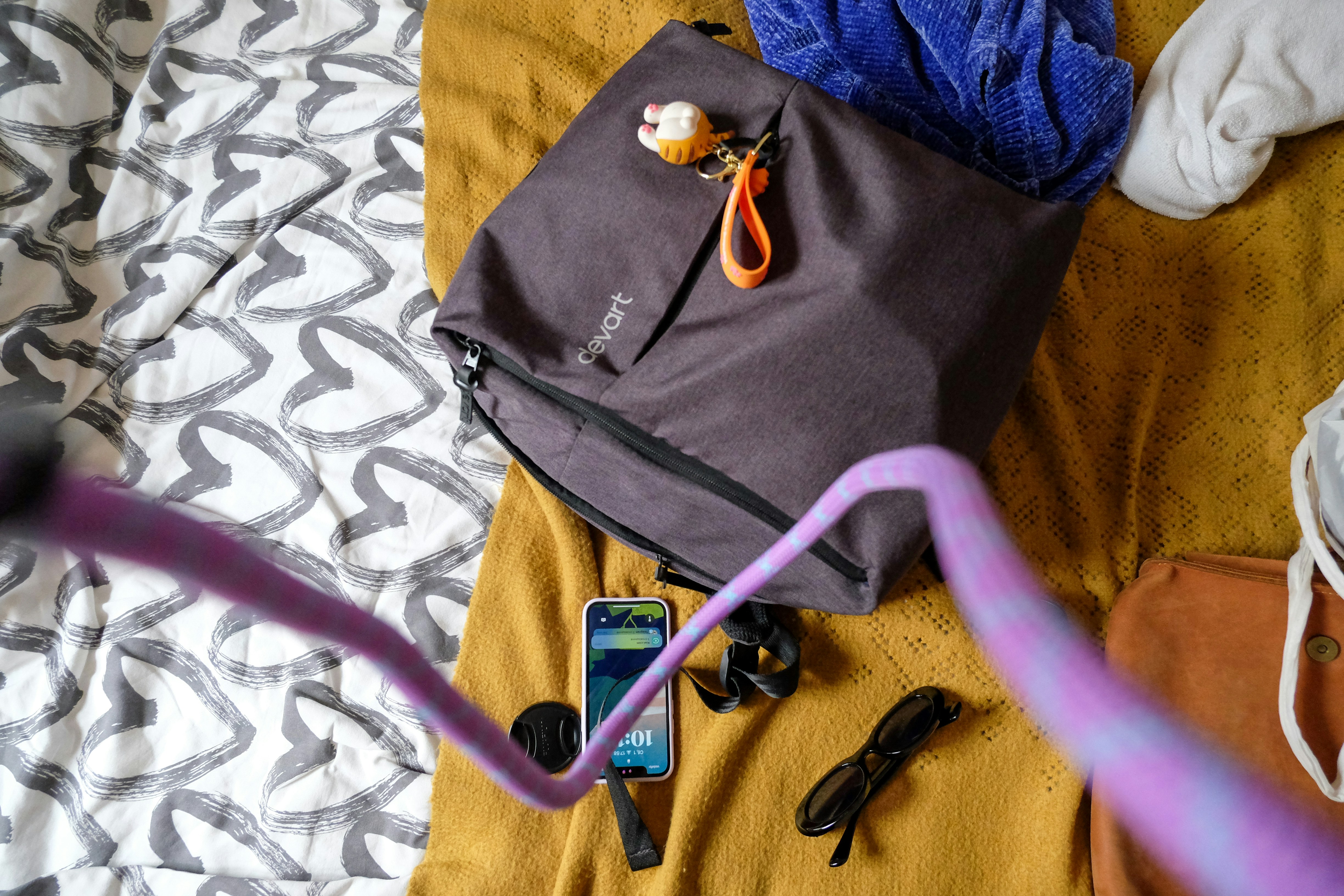 5 Carry-On Packing Hacks That Will Save You Time and Money – A bag, phone, and belongings are on a bed.