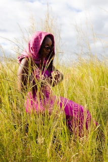 Woman in pink dress sits among tall grass.