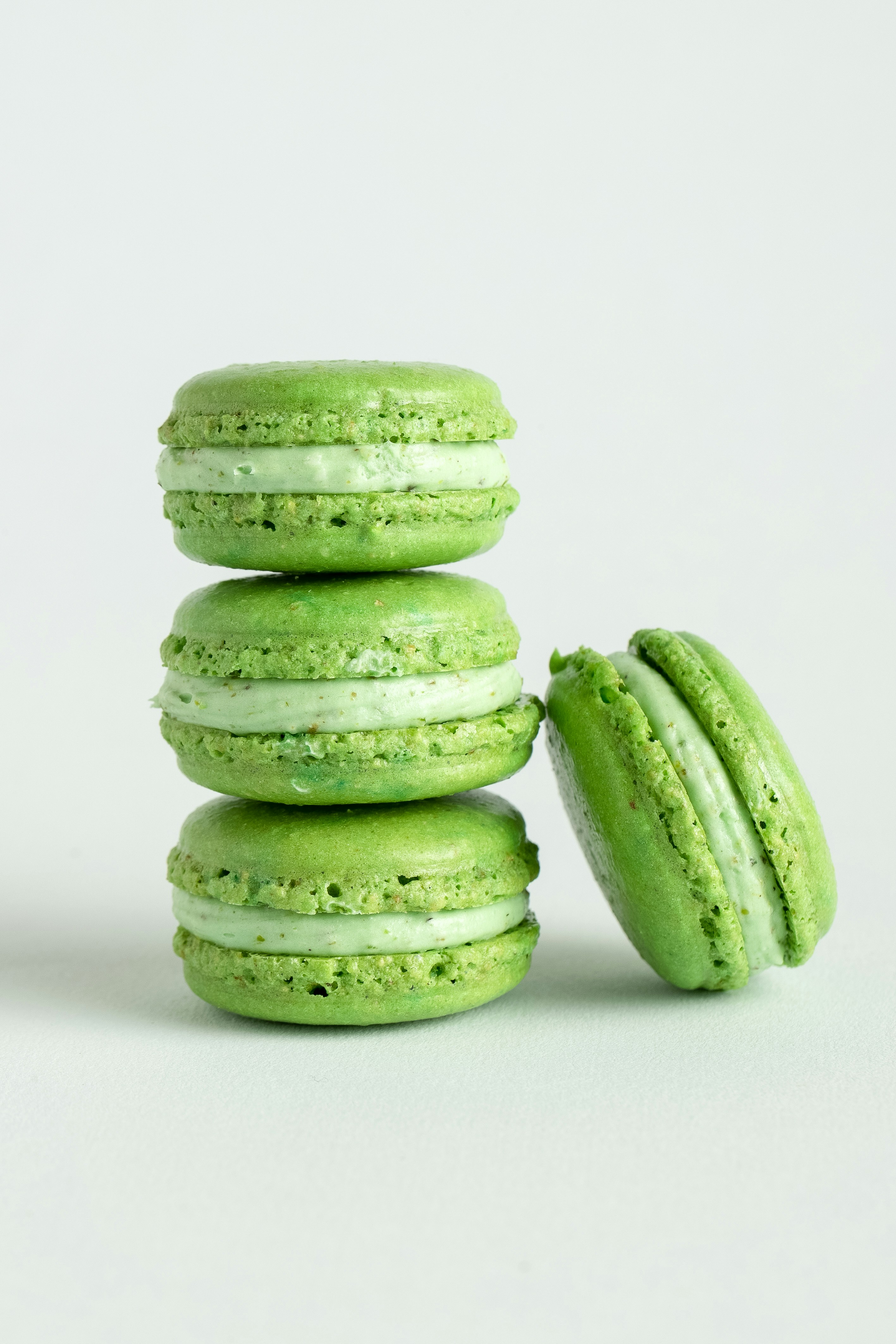 Here's a caption: green macarons are stacked on a white surface.