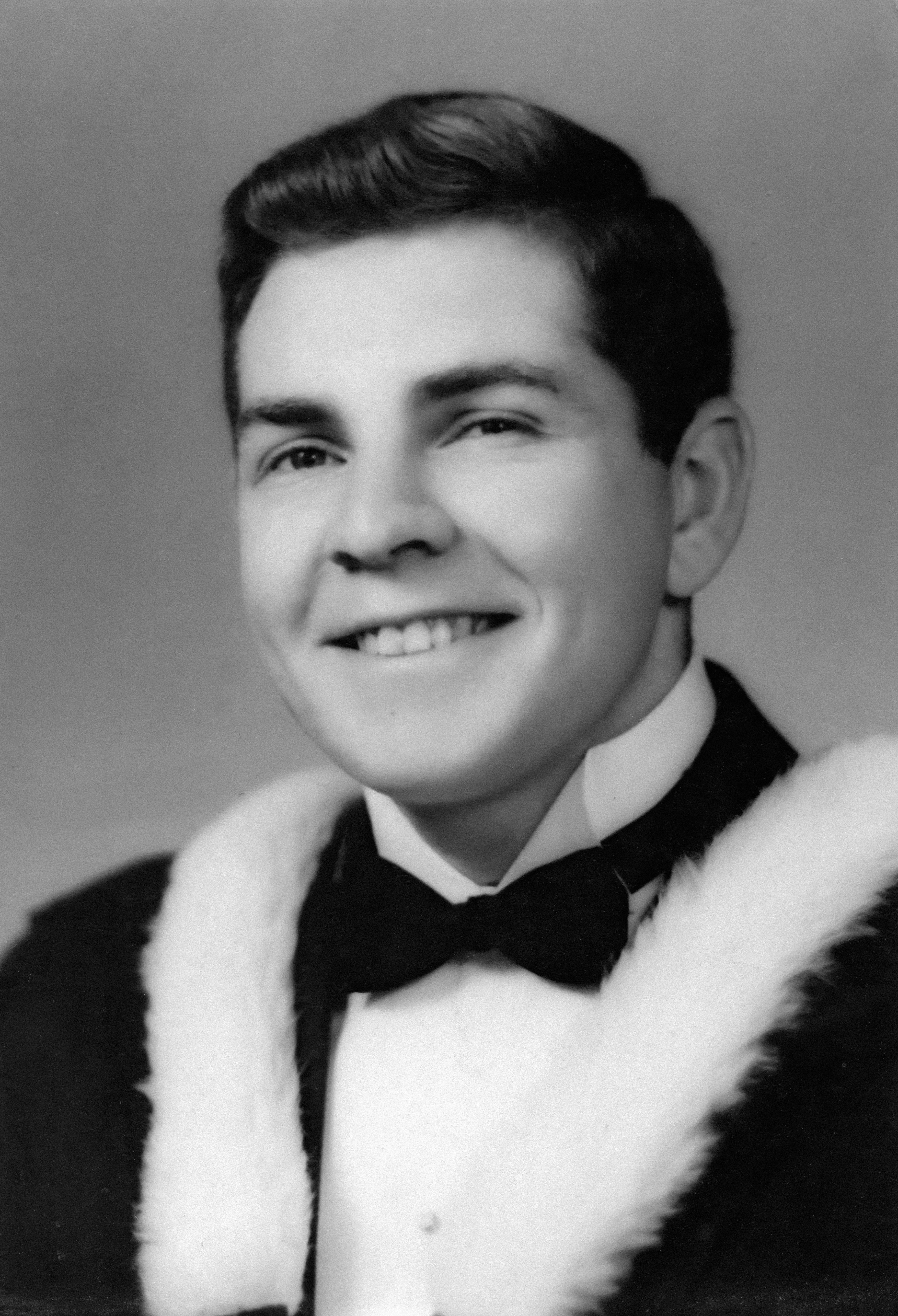 A smiling young man in formal attire and fur trim