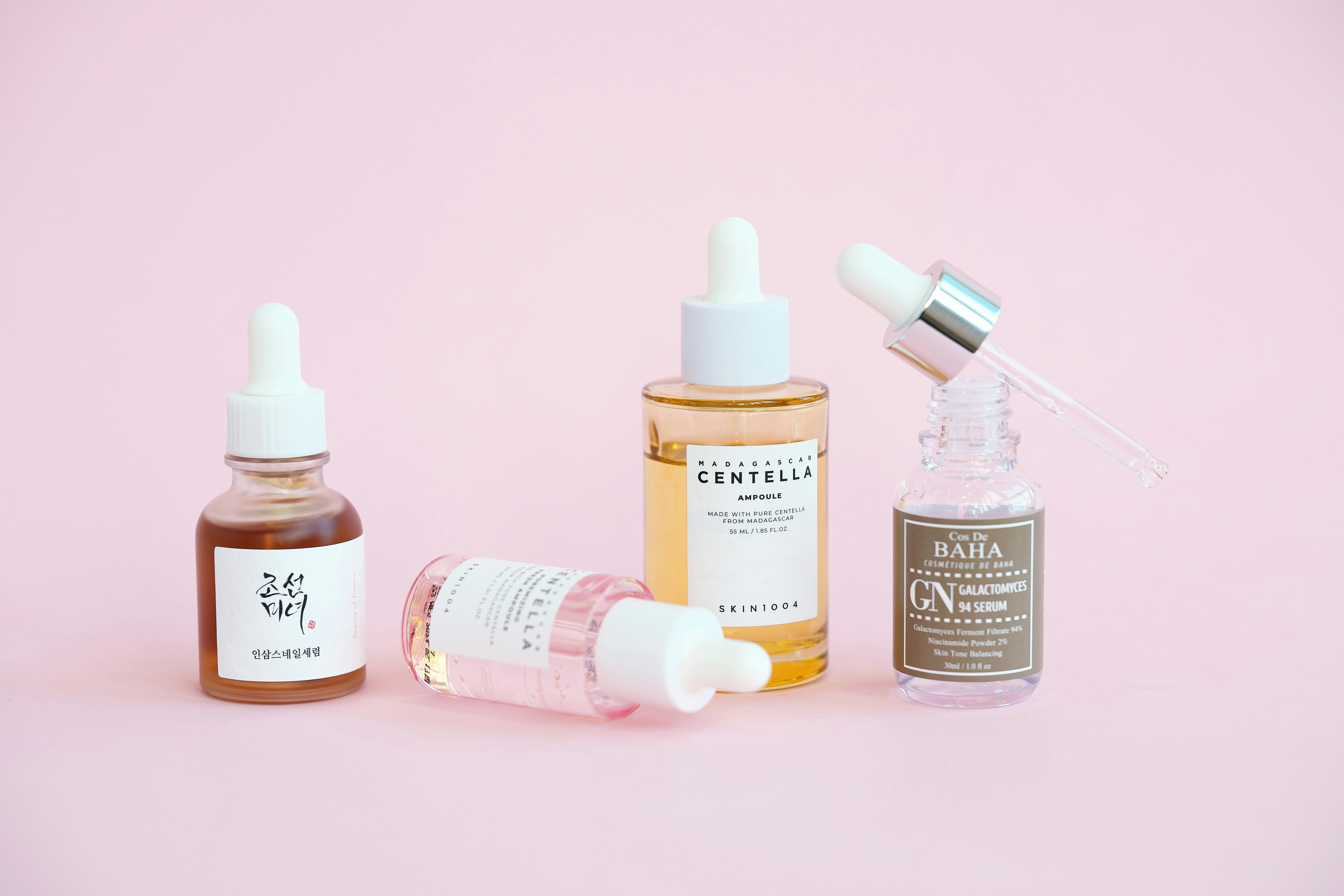 Skincare serums and dropper bottles sit on pink.