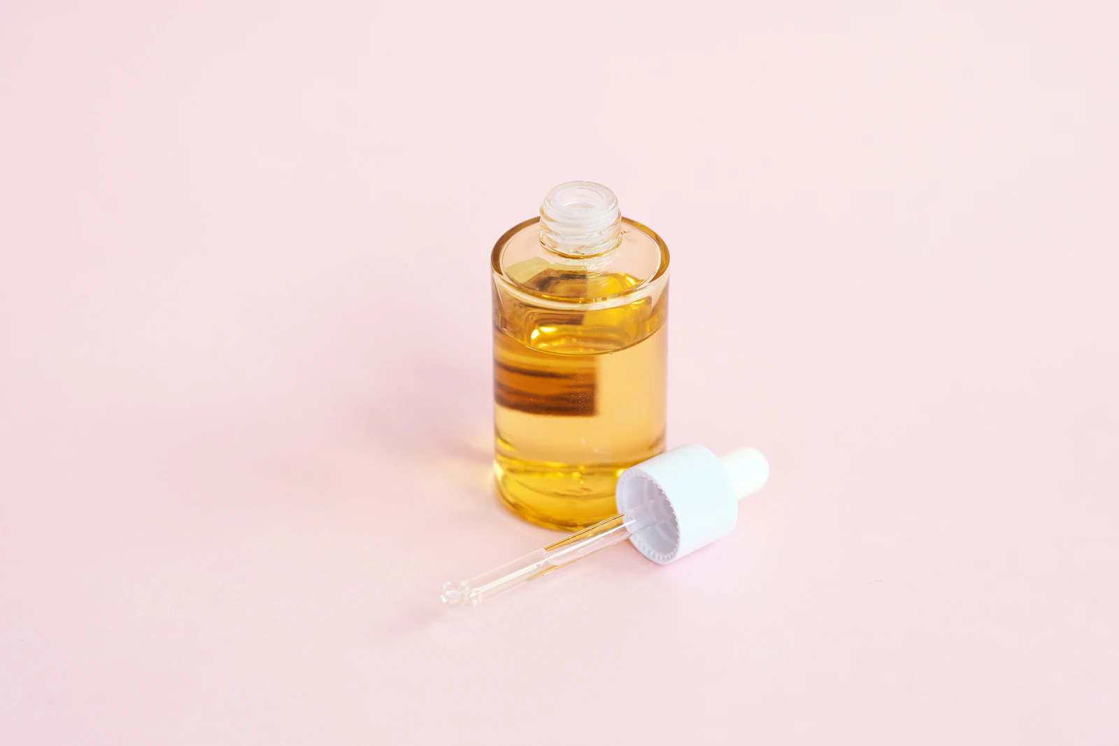 A skincare serum bottle and glass dropper resting on a pink surface, representing a hydrating serum comparison
