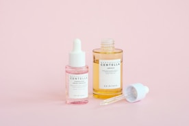Skincare serums are displayed on a pink background.