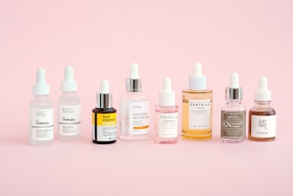 Skincare bottles are displayed on a pastel pink background.