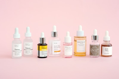 Skincare bottles are displayed on a pastel pink background.