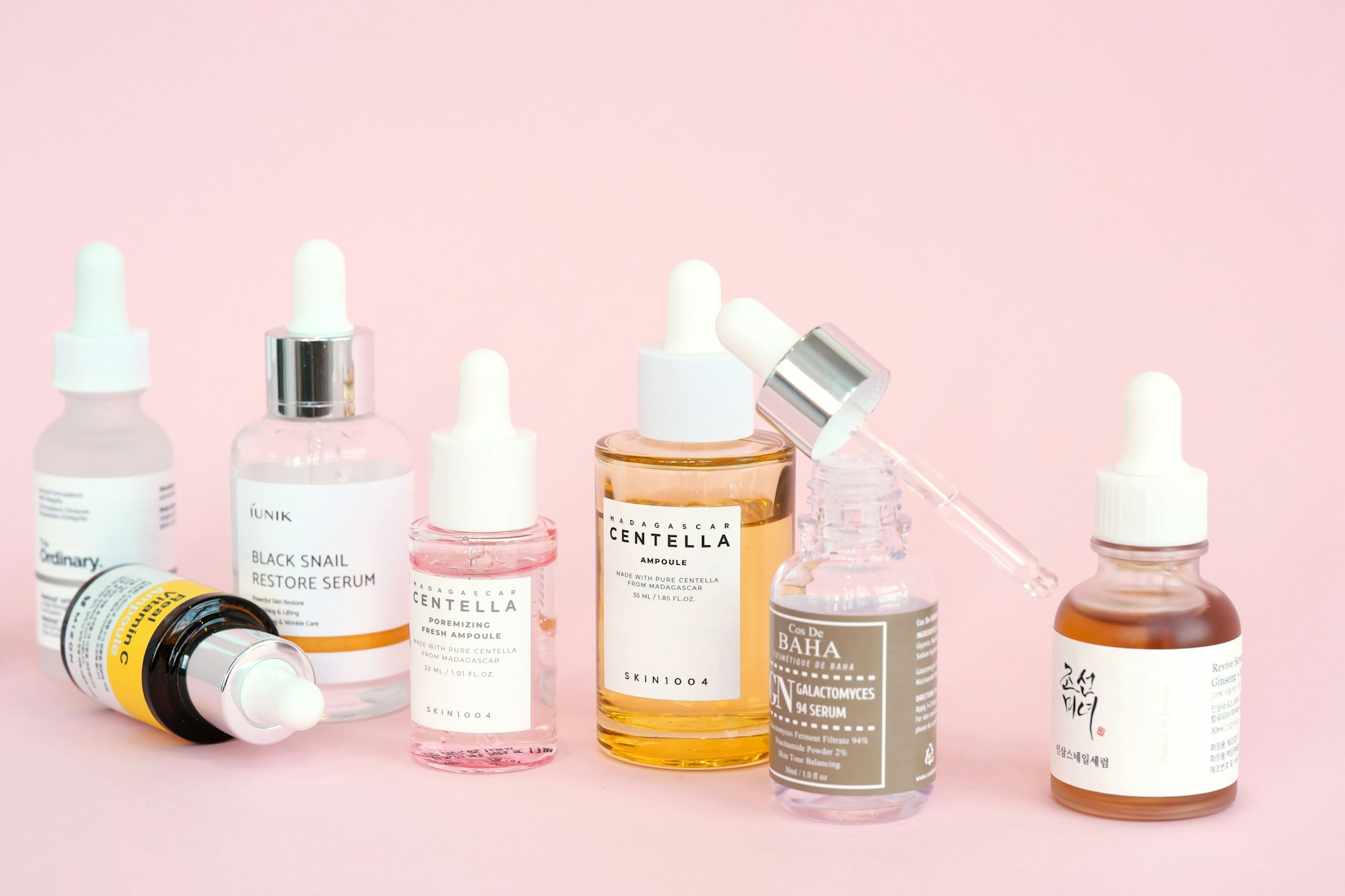 Skincare products, including serums, arranged on pink.